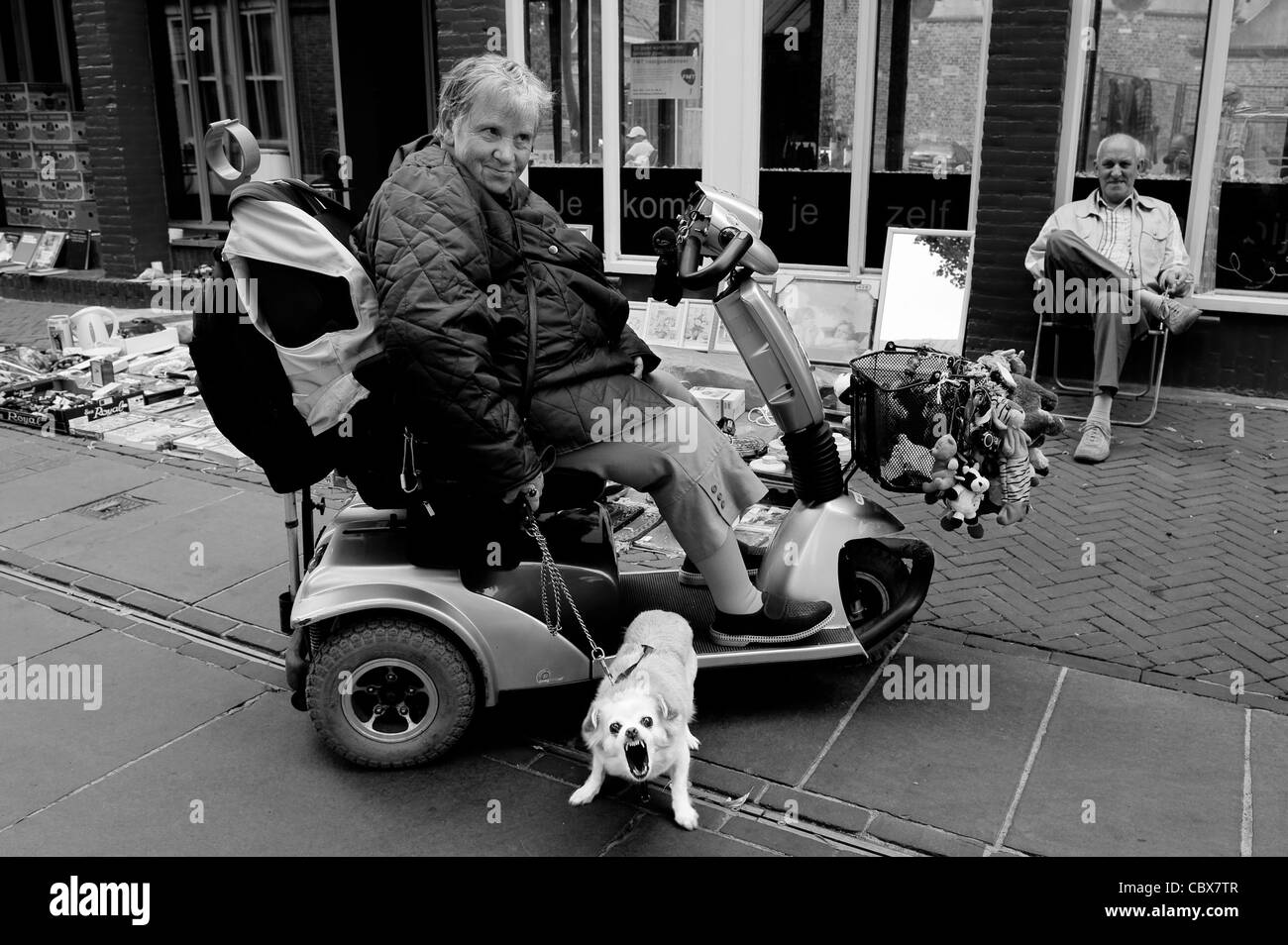 Enschede, Niederlande. Frau in einem Elektromobil mit Hund. Im Hintergrund ein Flohmarkt auf der Straße. Stockfoto
