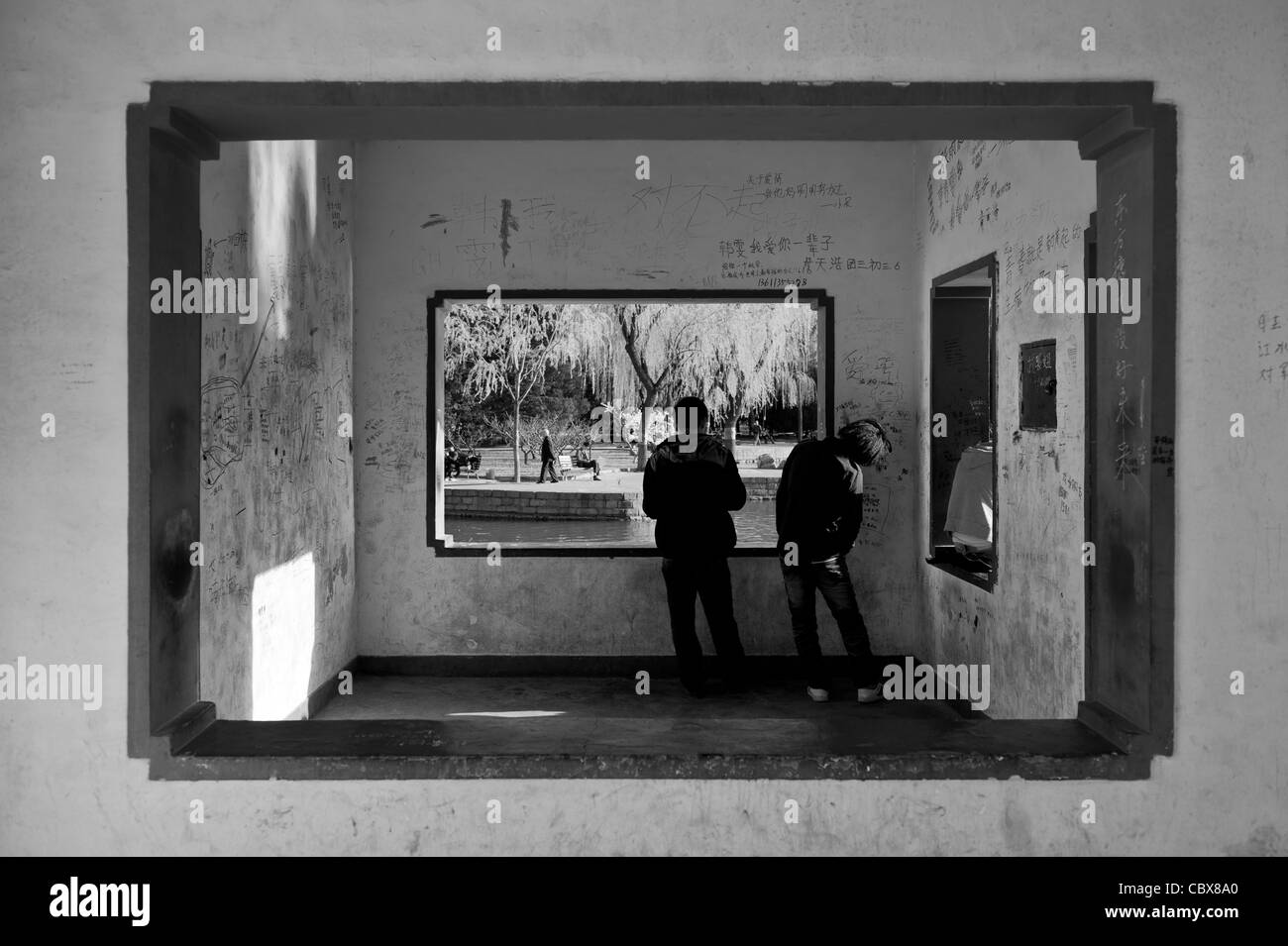 Beijing, Tuanjiehu Park. Zwei junge Mann Lesen der Texte von Graffiti an den Wänden eine Zuflucht in den Park. Stockfoto