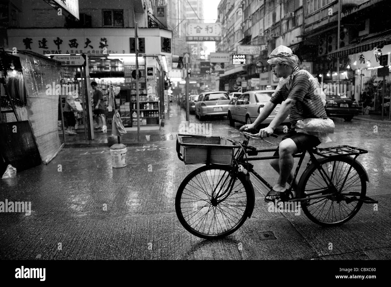 Kowloon, Hong Kong. Mann auf einem Fahrrad über die Straße bei starken Regenfällen. Stockfoto