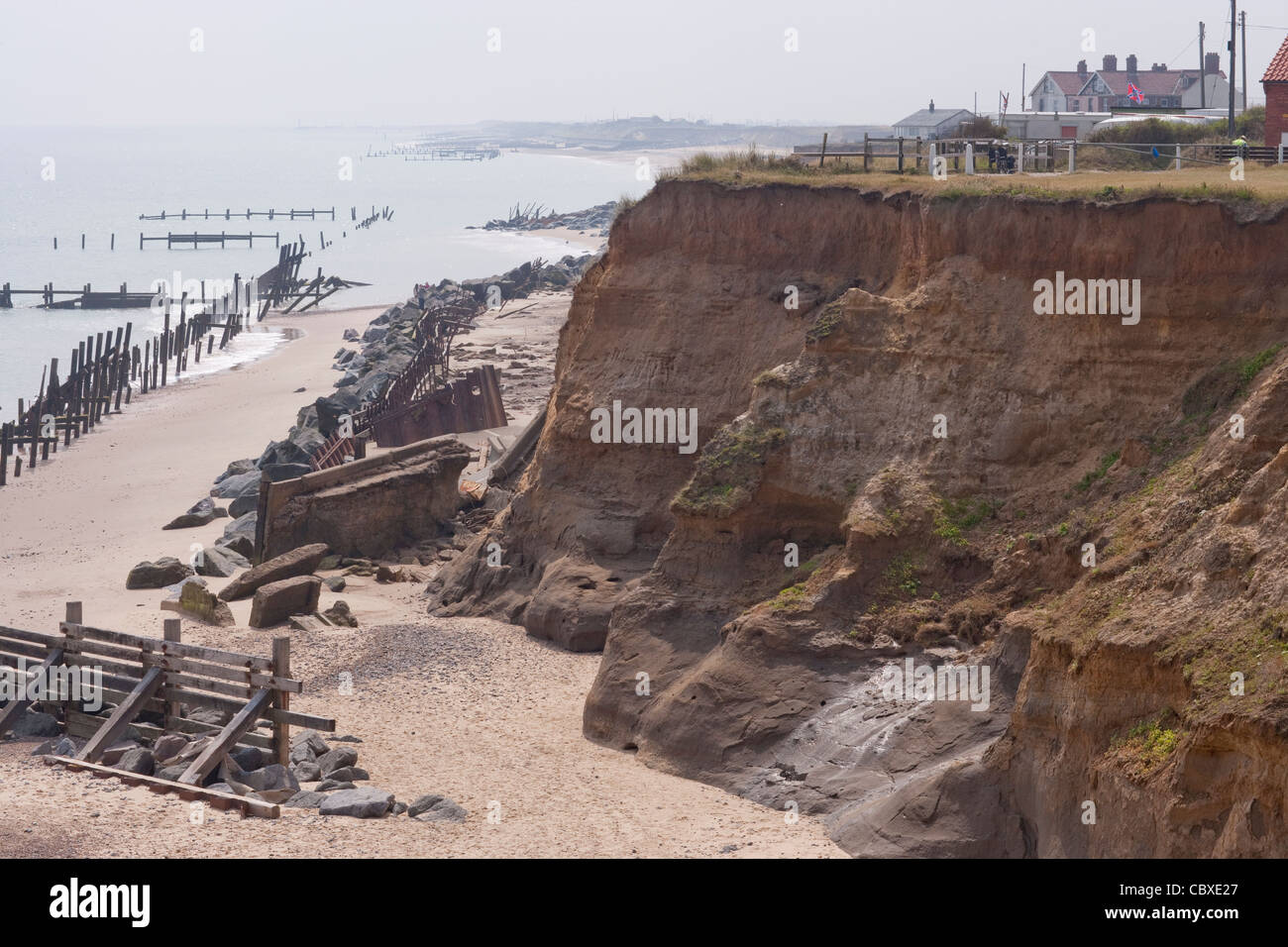 Happisburgh Küste, North Norfolk, East Anglia. Erosion der Felsen an der Nordsee; Häuser, weiter. Importierte Felsen unten Stockfoto