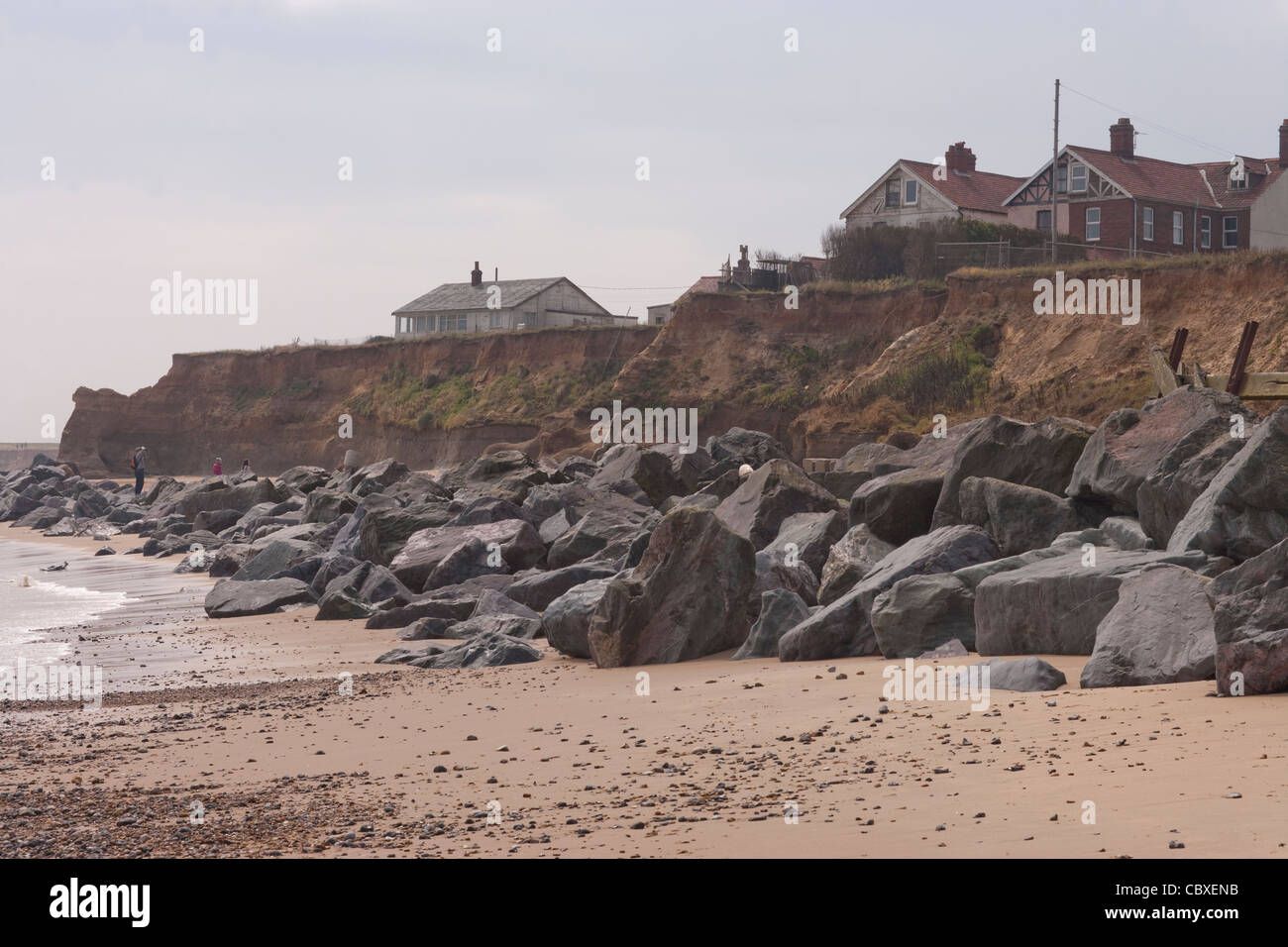 Happisburgh Küste, North Norfolk, East Anglia. Erosion der Felsen an der Nordsee; Häuser auf Klippe, importierte Felsen unten. Stockfoto