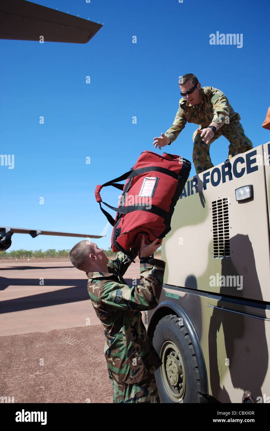 Senior Airman Shawn Pate übergibt Feuerausrüstung an den führenden Flugzeugführer der Royal Australian Air Force Liam Varley, Juli 19, im Bradshaw Field Training Area, Australien. LAC Varley lädt die Ausrüstung auf einem E-One Titan Feuerwehrmotor als Teil von Talisman Sabre 2009. Airman Pate ist ein Feuerwehrmann der 3. Zivilingenieursstaffel der Elmendorf Air Force Base, Alaska. LAC Varley ist ein Rettungsfeuerwehr in der Luftfahrt. Stockfoto