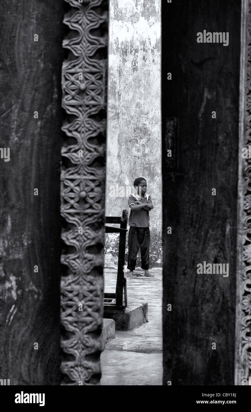 Ansicht eines afrikanischen jungen durch eine Tür stehen bereit mit seinen Händen überquerte in einem Hof in Stonetown, Zanzibar Stockfoto