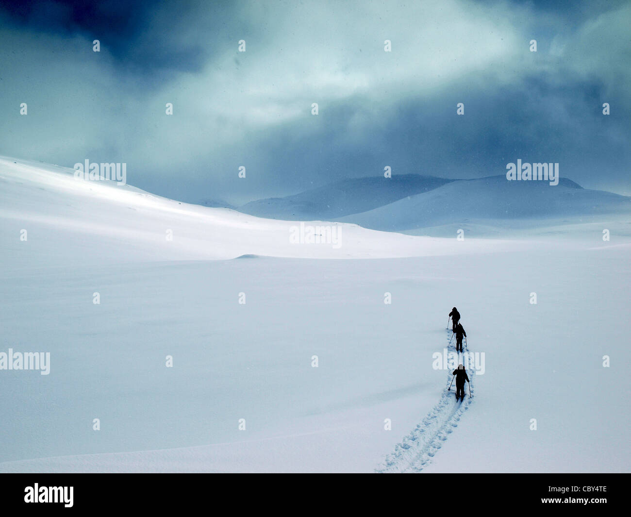 3 Skitourengeher brechen Weg in neue Schnee-Kopf in Richtung fernen Hügel unter einem bedrohlichen Himmel in Nord-Norwegen Stockfoto