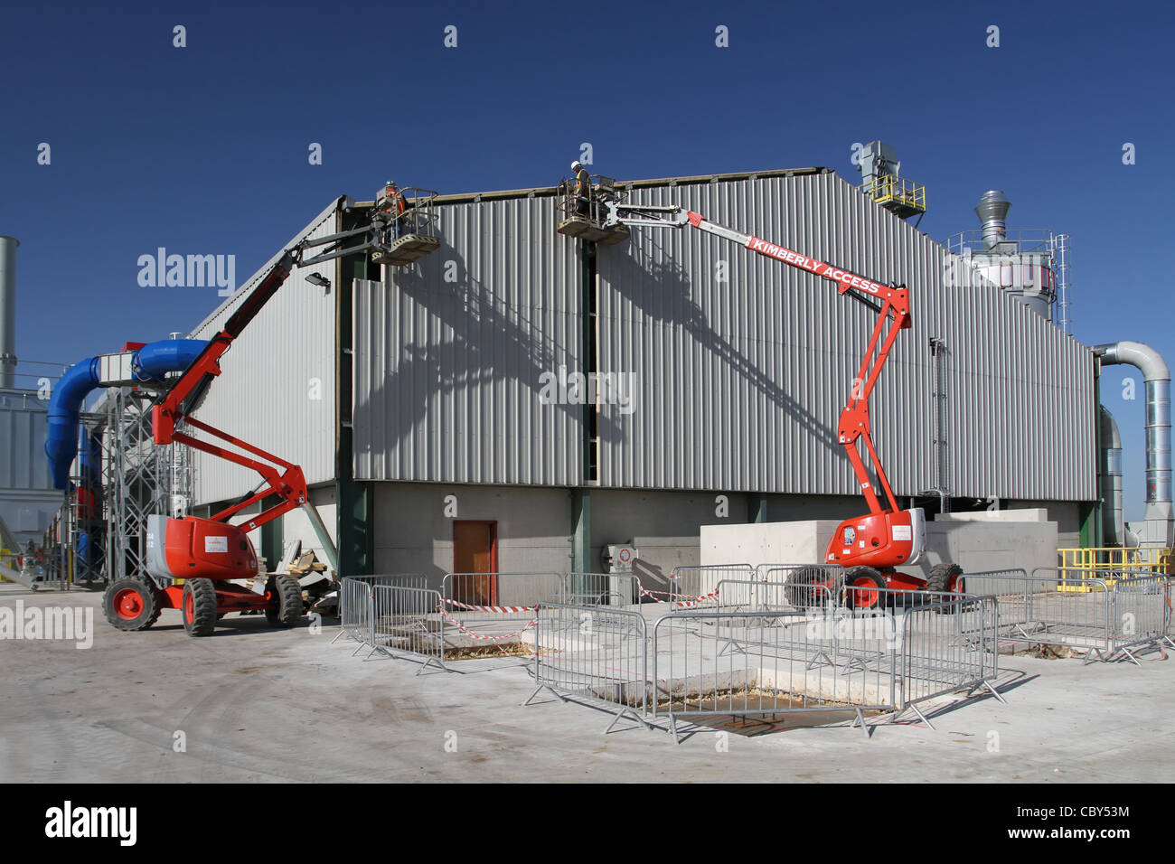 2 Männer in Cherry Pickers auf eine neue Industrieanlage Stockfoto