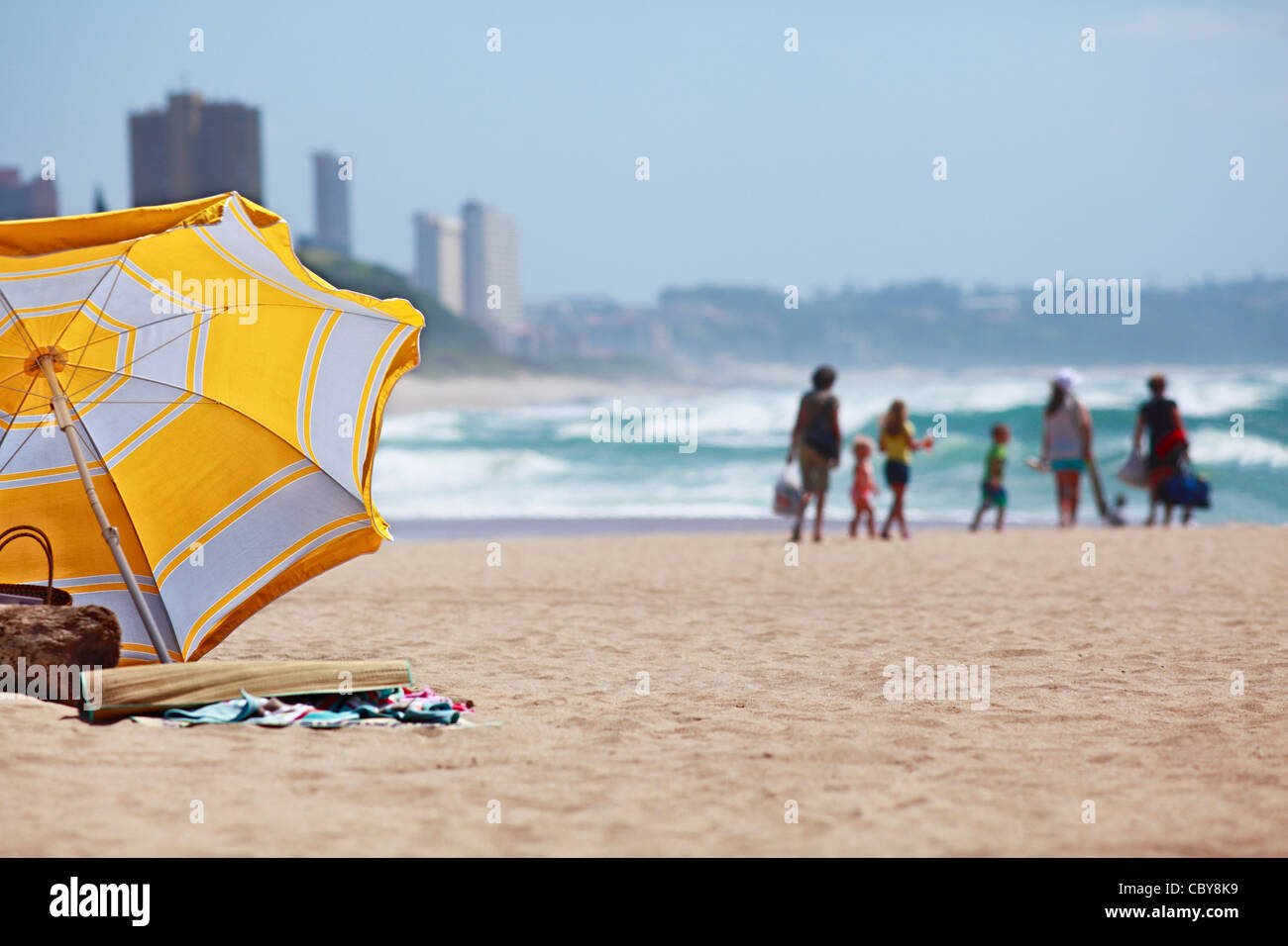 Sommer Urlaub am Meer. Sonnenschirm im Vordergrund und ein Groupf von Menschen in der Diastance. South Coast, Südafrika. Stockfoto