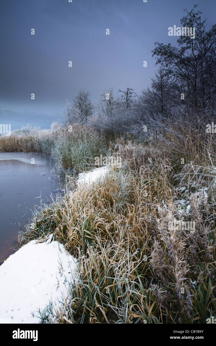 Eine dunkle Schnee gefüllt Himmel über einen gefrorenen Teich in der englischen Landschaft Stockfoto