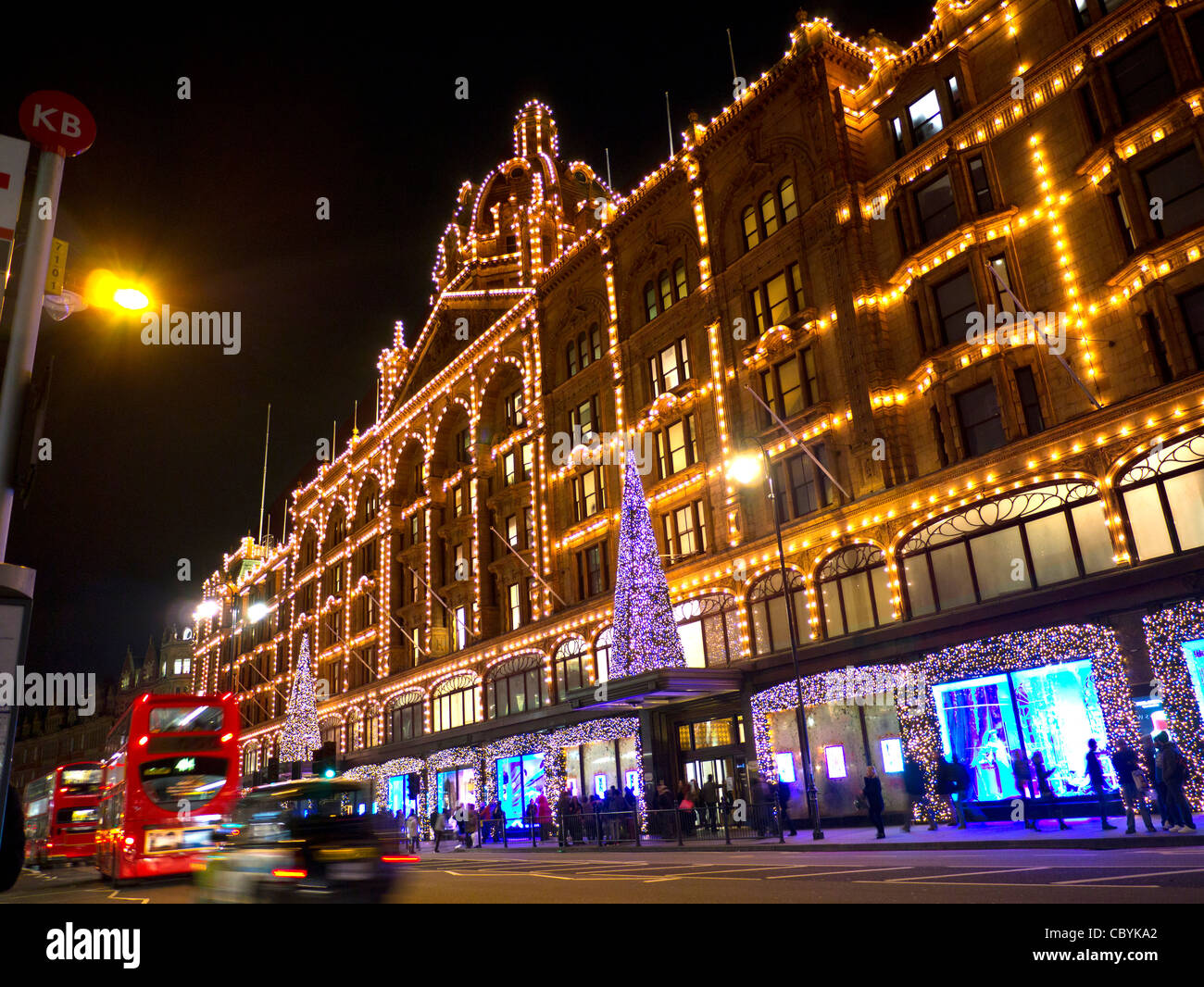 Weihnachten Einkaufen in London Harrods Kaufhaus in der Dämmerung mit Weihnachtsbeleuchtung Shopper und vorbeifahrenden Taxis und rote Busse Knightsbridge London SW1 Stockfoto