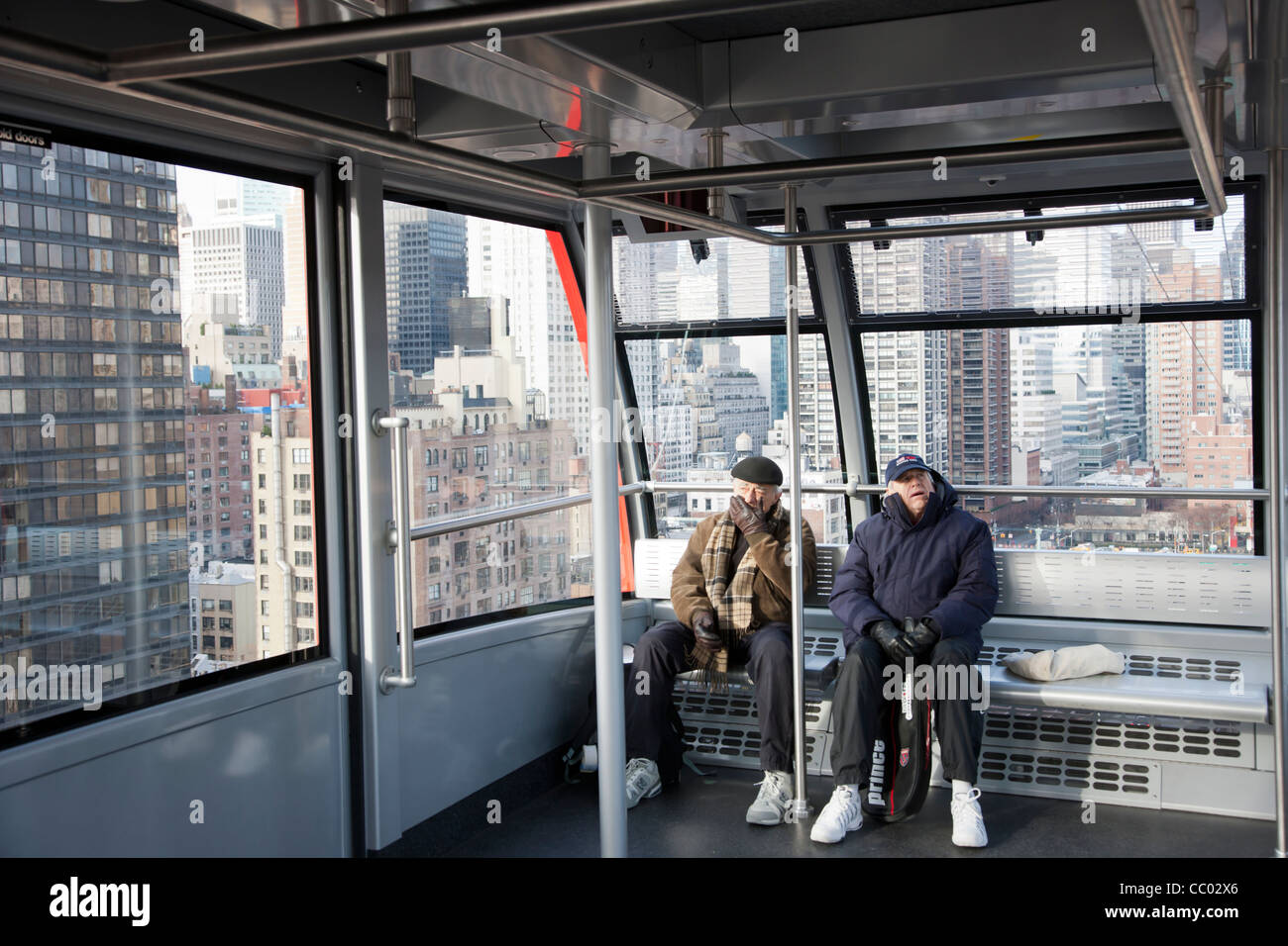 Zwei Passagiere an Bord geleitet die Roosevelt Island Tram für Roosevelt Island, mit der East Side von Manhattan im Hintergrund Stockfoto