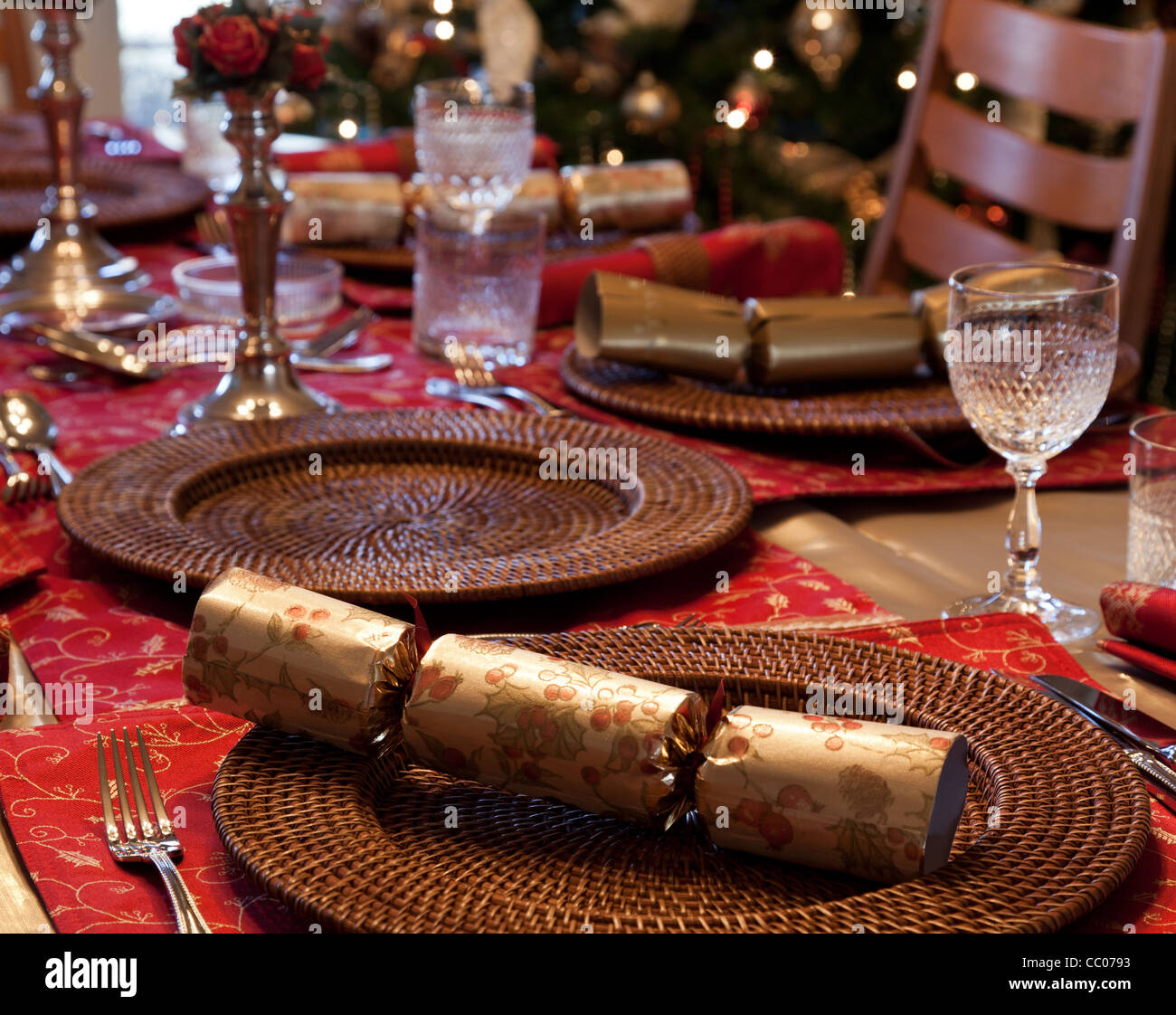 Christmas Cracker am Tisch für Weihnachtsessen mit Kerzen und Baum im Hintergrund Stockfoto