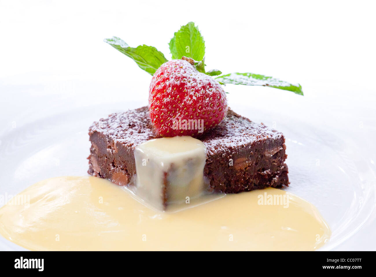 Schokoladen-Brownie Slice mit Erdbeer und serviert mit Vanillesoße Stockfoto