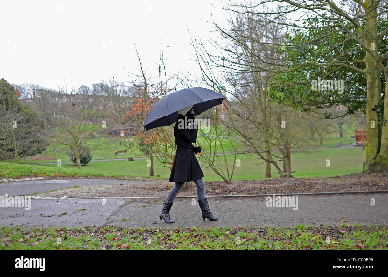 Junge Frau mit großen schwarzen Regenschirm in einem Park Brighton bei nassem Wetter UK Stockfoto