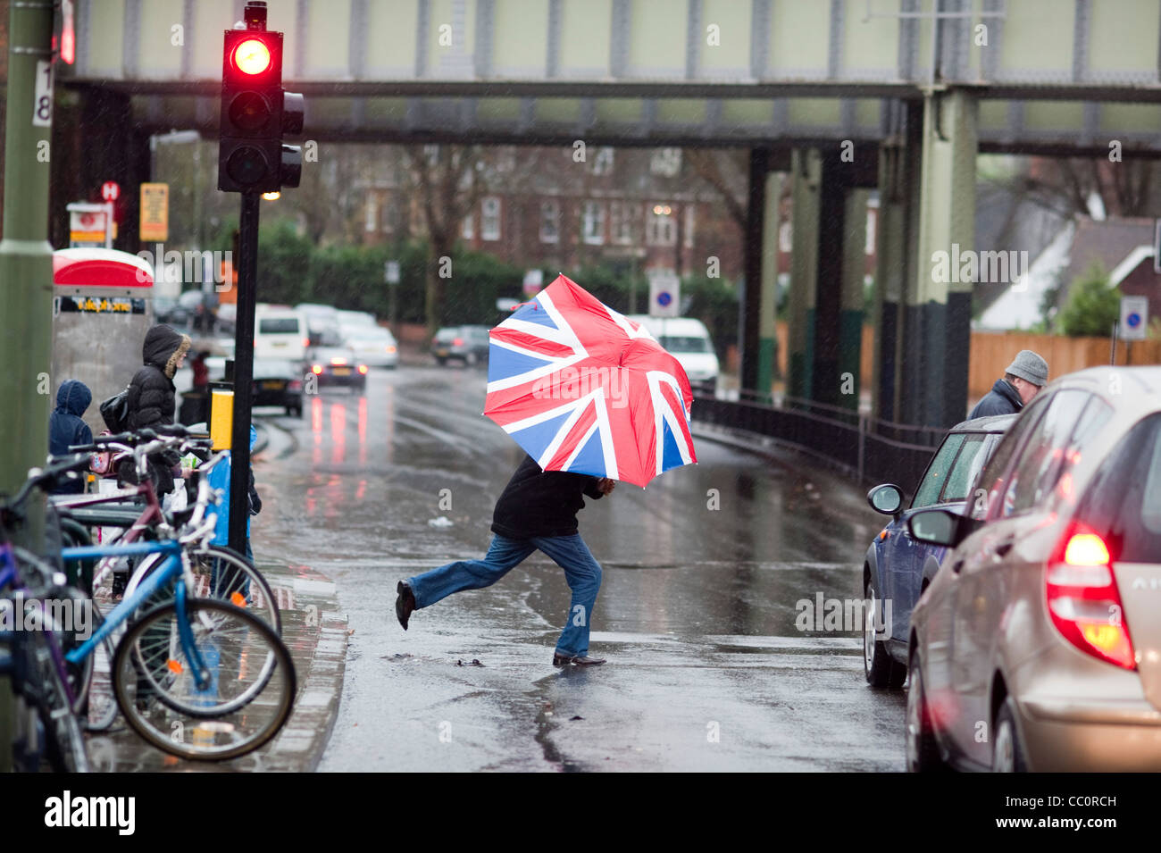 Mann mit Union Jack Regenschirm überquert die Straße Stockfoto