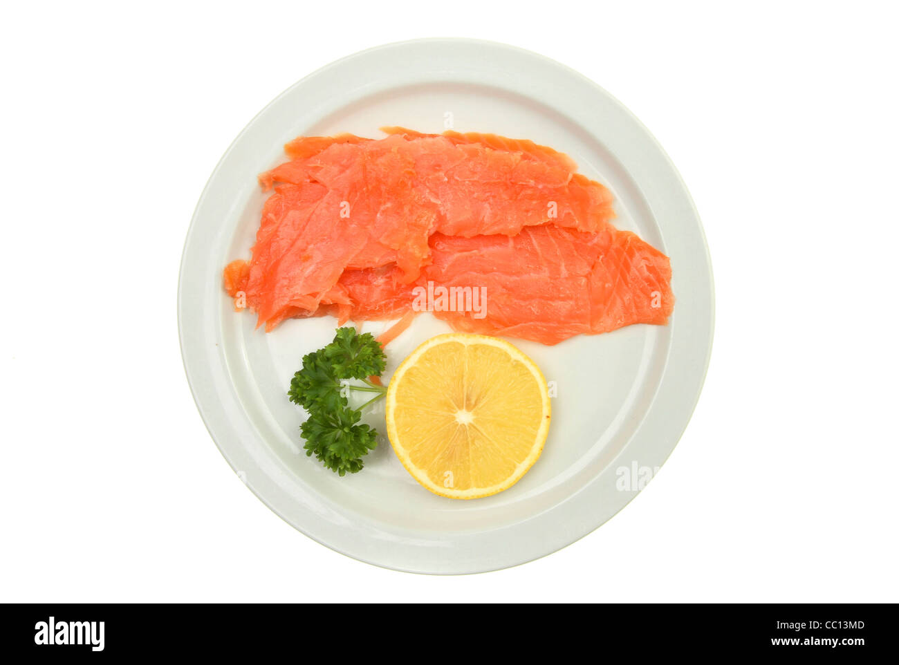 Geräucherter Lachs mit Petersilie und Zitrone auf einem Teller isoliert gegen weiß Stockfoto