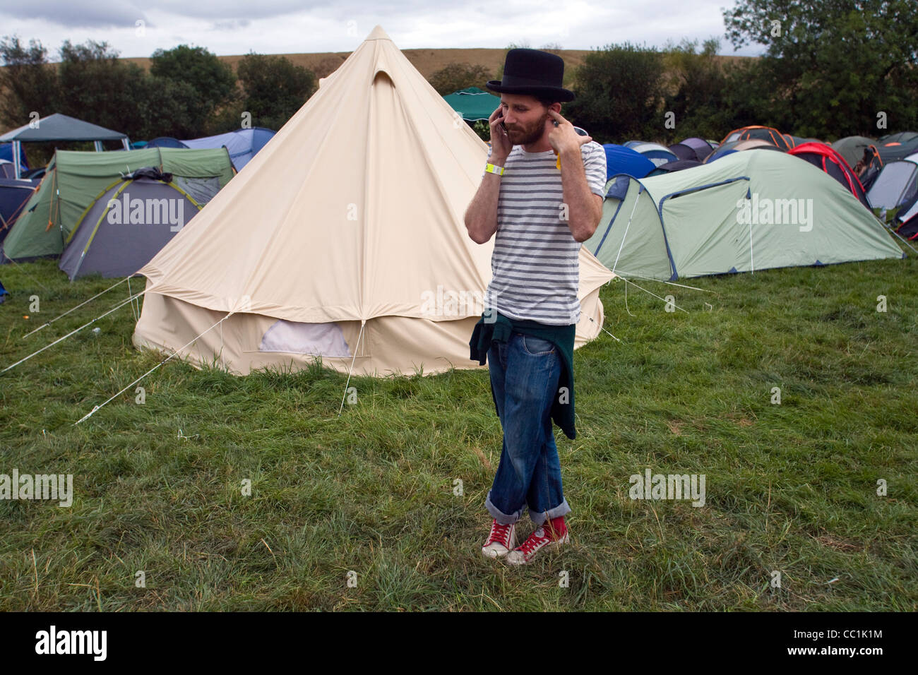 Ein Mann macht einen Anruf auf seinem Handy Mobiltelefon neben einem Feld von Zelten auf dem Standon Calling Festival Stockfoto
