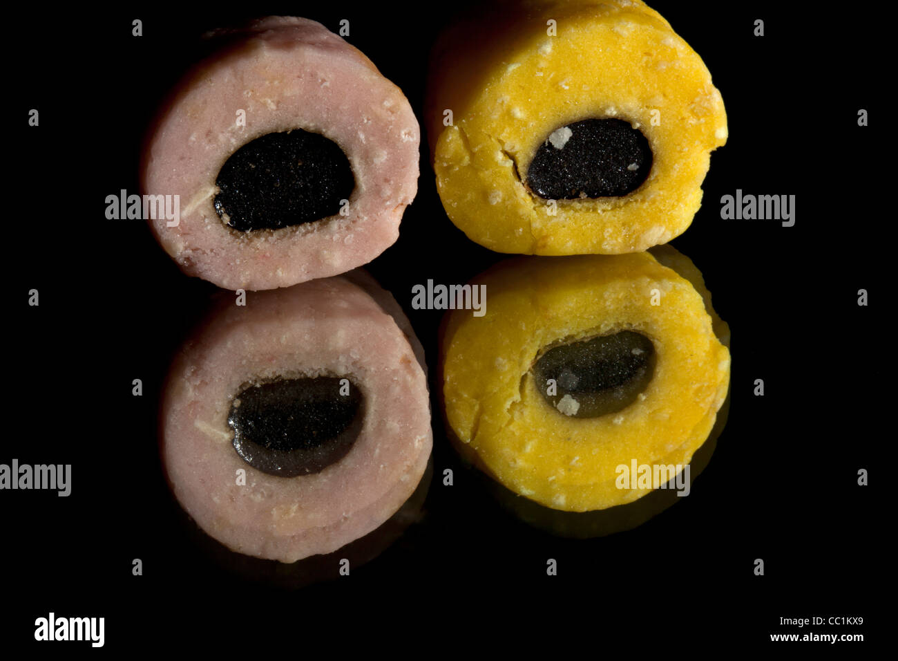 Zwei Lakritz Allsort Süßigkeiten (eine rosa und schwarz und die andere gelb und schwarz) auf einem schwarzen Hintergrund mit Reflexionen Stockfoto