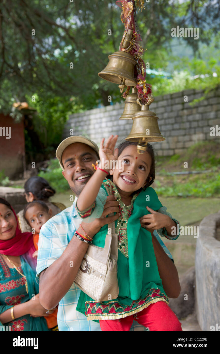Lächelnder Mann heben seine Tochter um die Tempel Glocken am Schrein gewidmet Gatotjaca, Himachal Pradesh, Indien Stockfoto