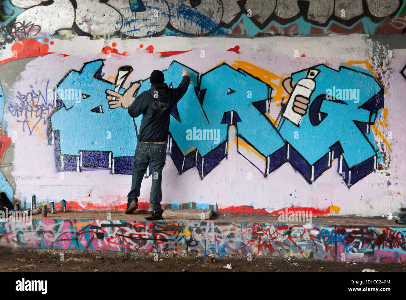 Tagging - Kapuzen-junger Mann Spray Malerei Graffiti unter Brücke. Stockfoto