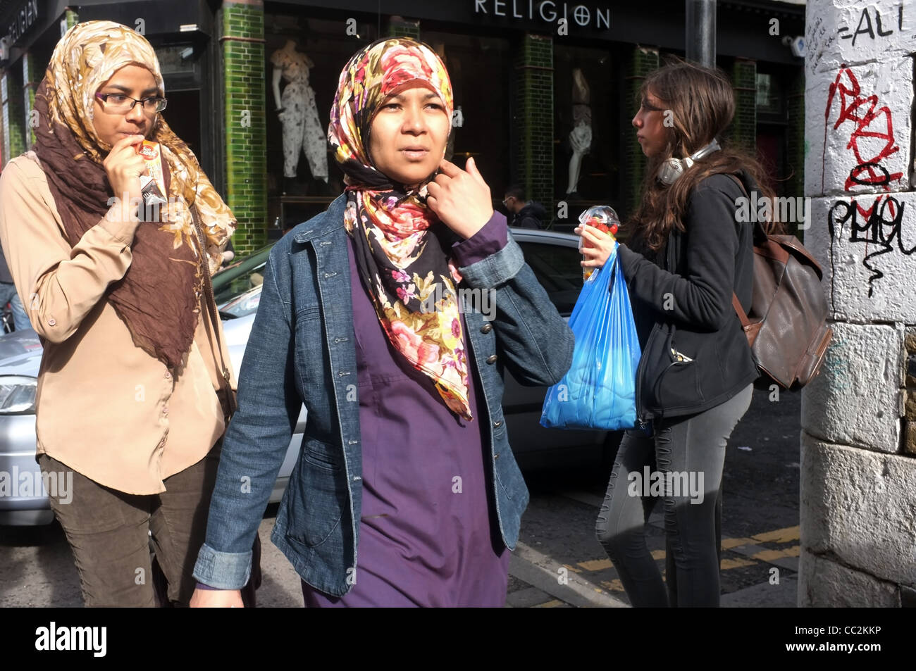 Zwei junge muslimische Frauen in Kopftüchern, entlang der Brick Lane, im historischen East End von London. Stockfoto