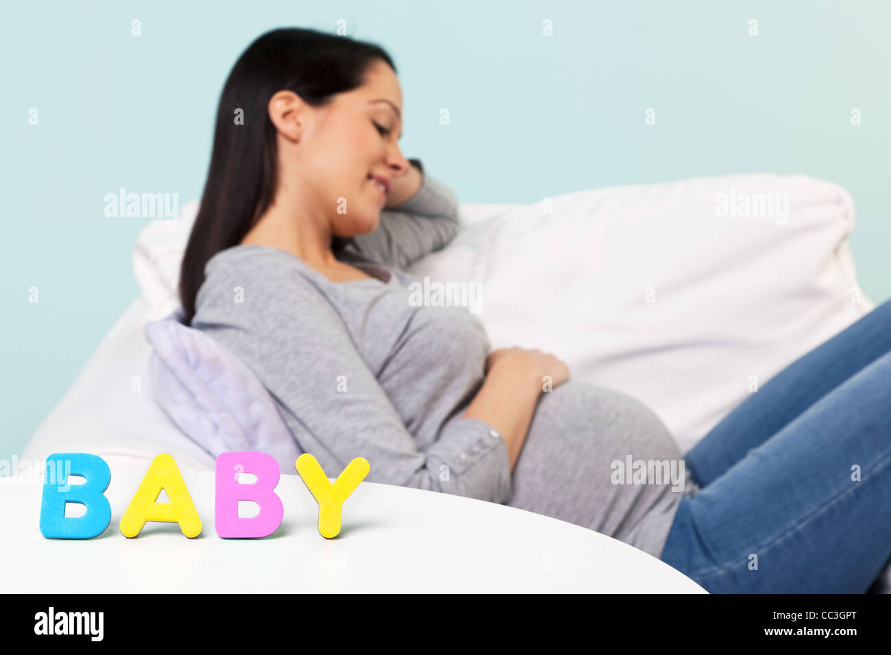 Foto von einer schwangeren Frau zu Hause sitzt in einem Sessel, Konzentration auf das Wort "BABY" auf dem Tisch vor. Stockfoto