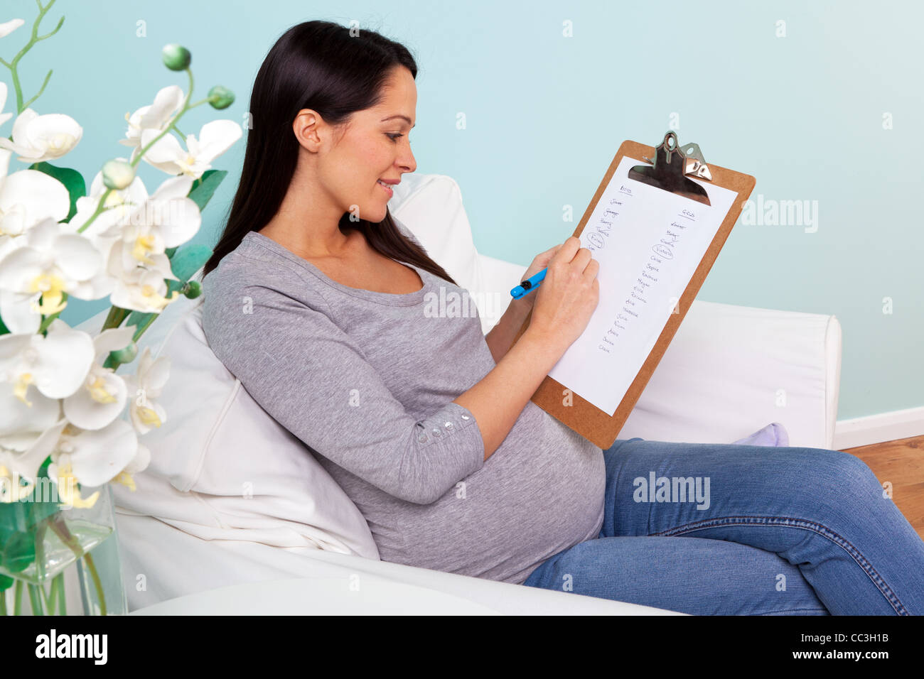 Foto von einer schwangeren Frau zu Hause sitzt in einem Sessel, schreiben eine Liste der möglichen jungen und Mädchen Namen für ihr Baby. Stockfoto
