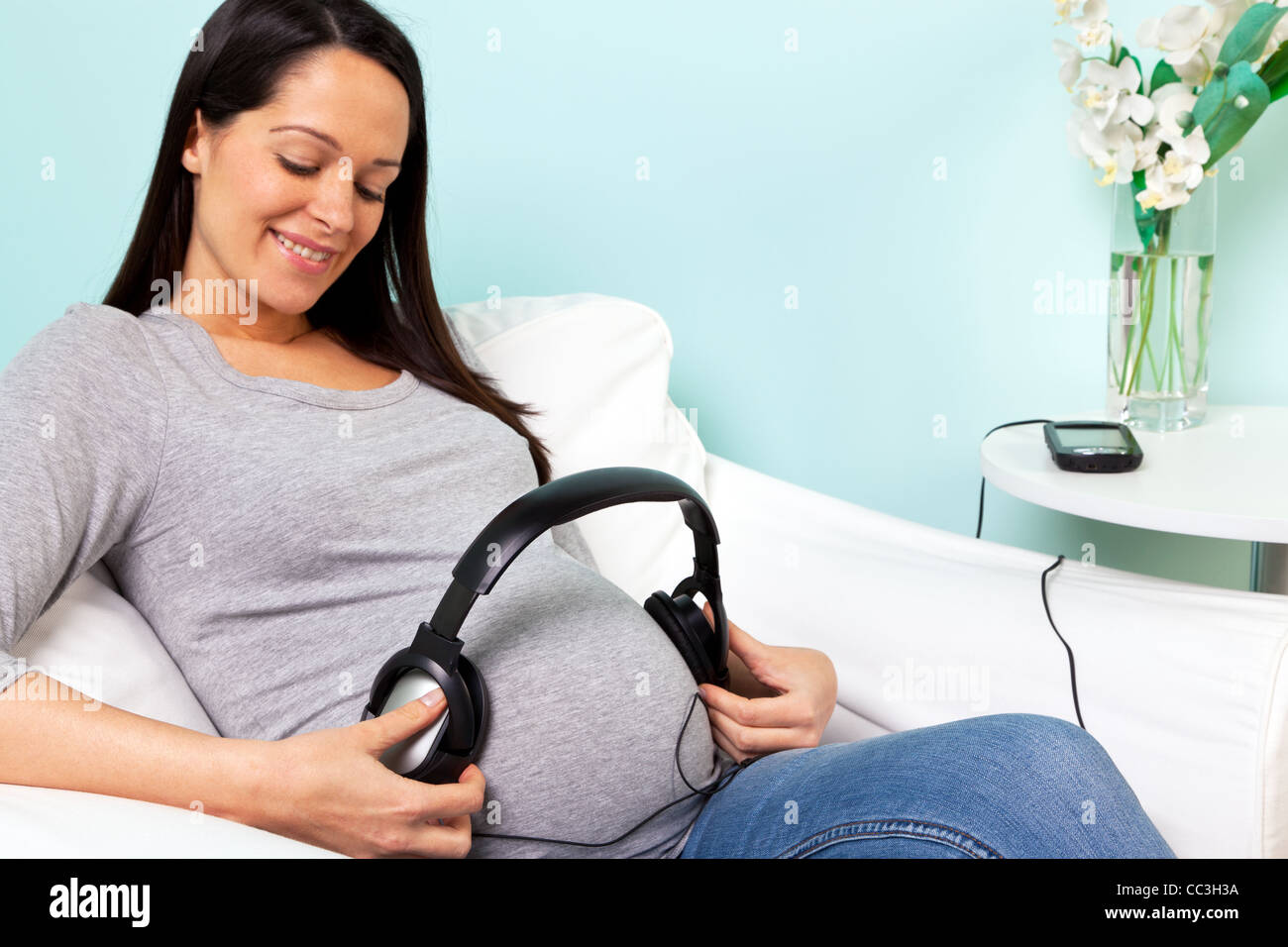 Foto von einer schwangeren Frau zu Hause sitzt in einem Sessel, die Wiedergabe von Musik über Kopfhörer auf ihr baby Stockfoto