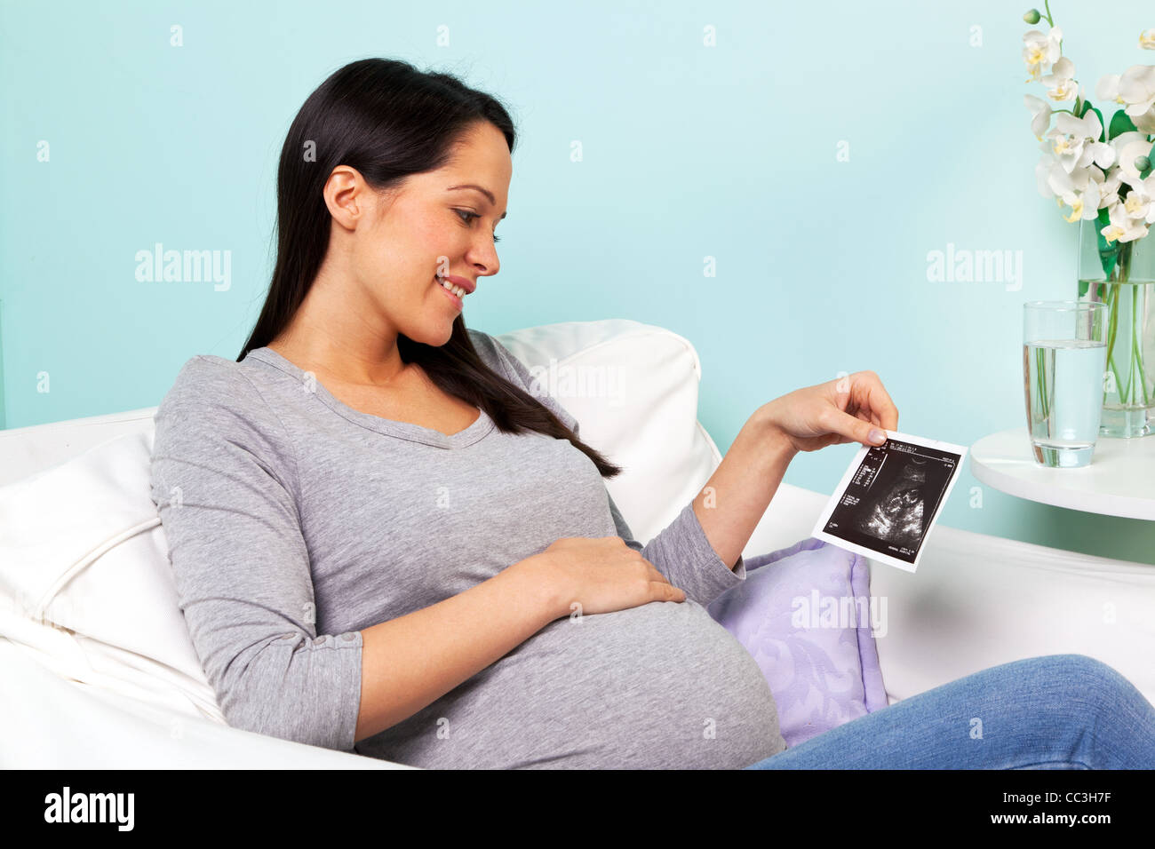 Foto von einer schwangeren Frau zu Hause sitzt in einem Sessel, Blick auf ihr Baby-Ultraschallbild drucken. Stockfoto