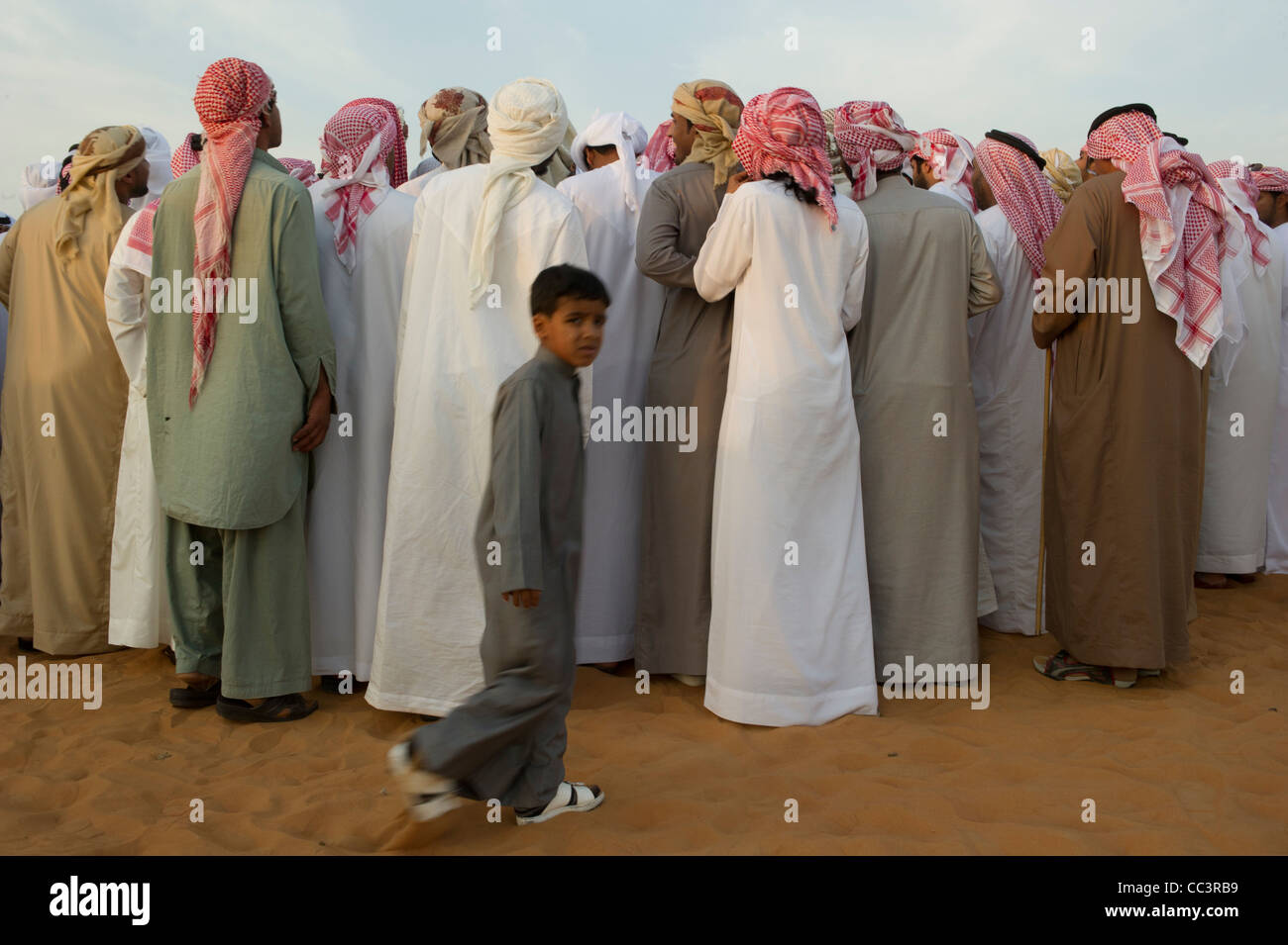 Ein kleiner Junge auf der nach außen eine Schar von arabischen Männern beobachtete eine Präsentation der Kamelzucht Stockfoto