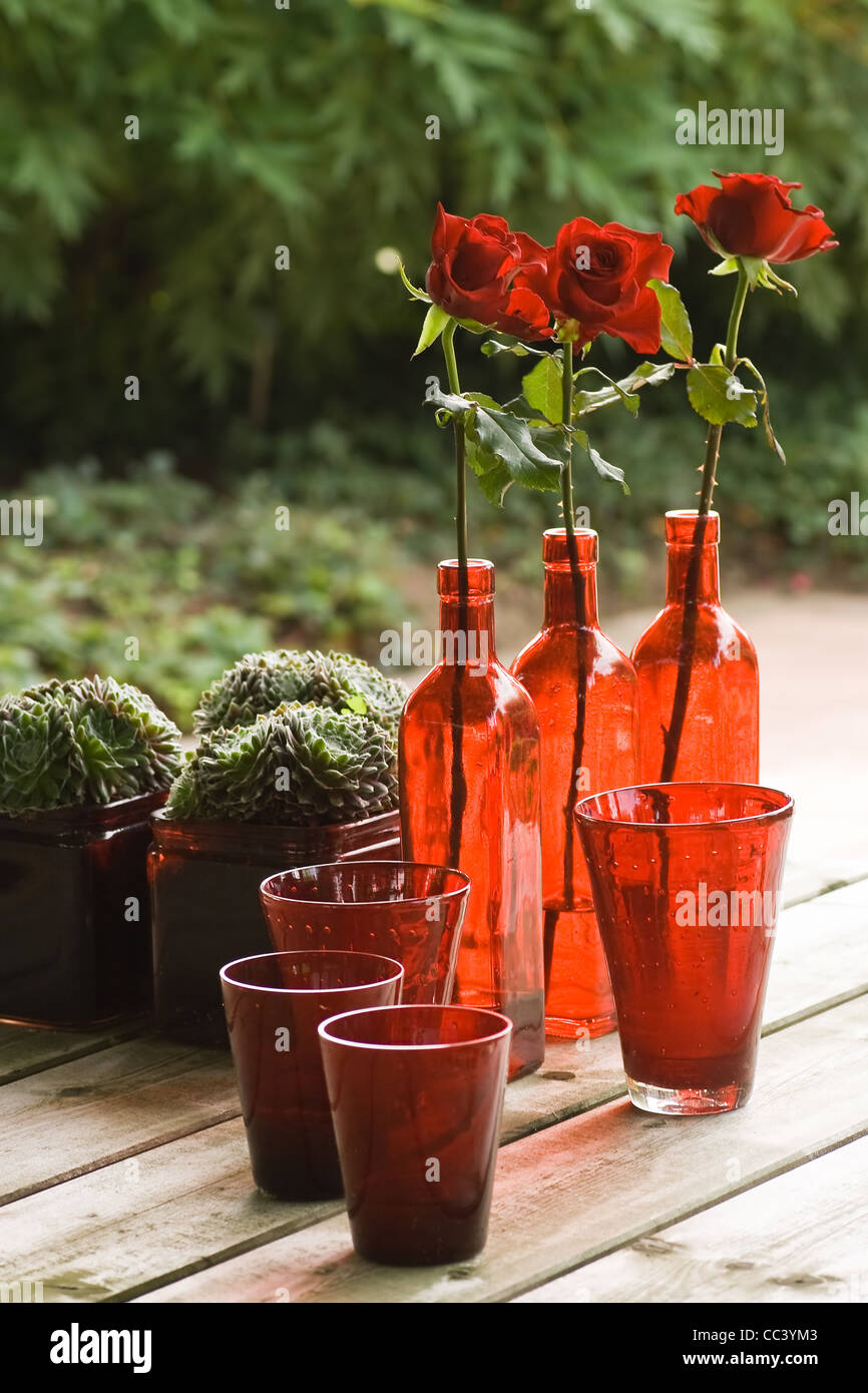 Tische im Garten mit Stillleben, Rotes Glas, Pflanzen und Rosen Stockfoto