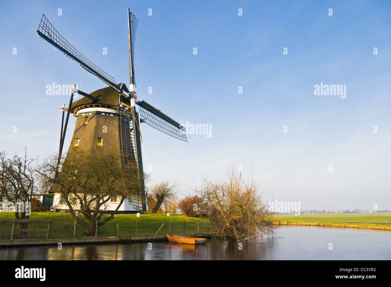 Holländische Polderlandschaft mit Windmühle und Boot über das Einfrieren kalten sonnigen Wintertag Stockfoto