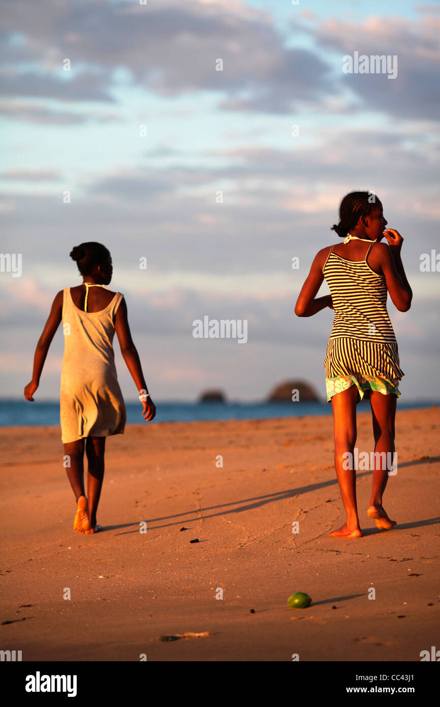 Zwei junge madagassische Frauen Fuß am Strand in Ampangorinana, Nosy Komba, Nordwest-Madagaskar, Afrika, bei Sonnenuntergang. Stockfoto