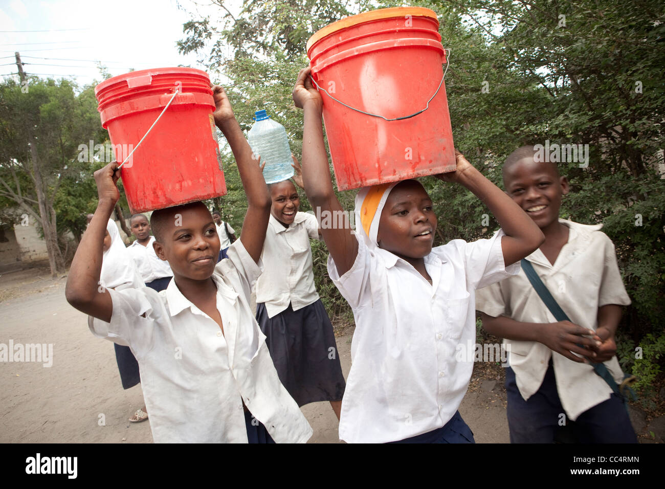 Schüler tragen Wasser wieder aus dem Brunnen in Dar Es Salaam, Tansania, Ostafrika. Stockfoto
