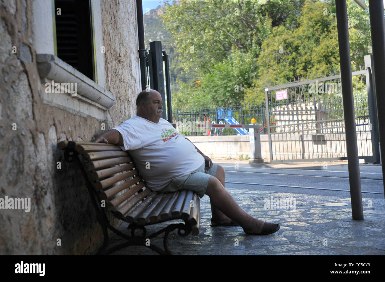 Ein großer Mann sitzt an einem heißen Tag im Schatten vor Bahnhof Soller auf Mallorca Stockfoto
