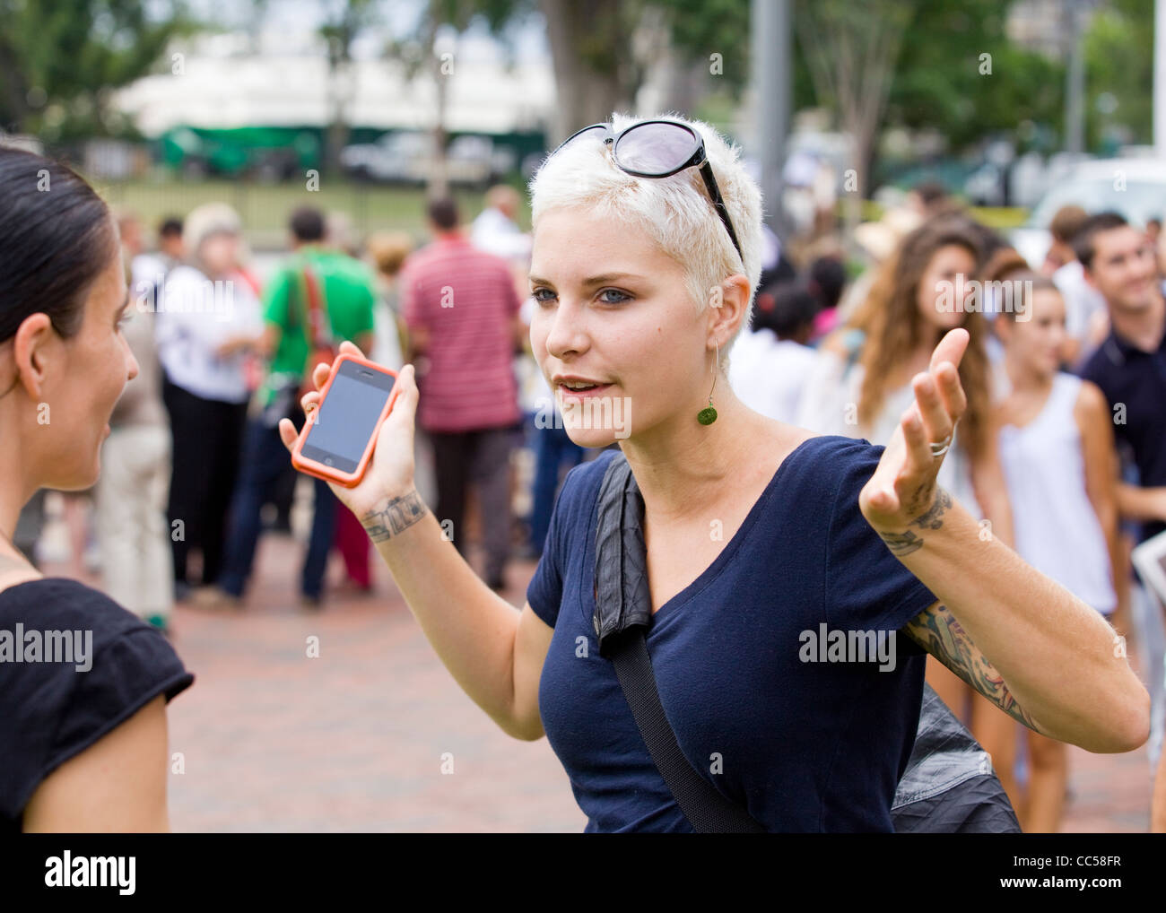 Eine junge, blonde Frau wirft ihre Hände beim sprechen mit einem Freund Stockfoto