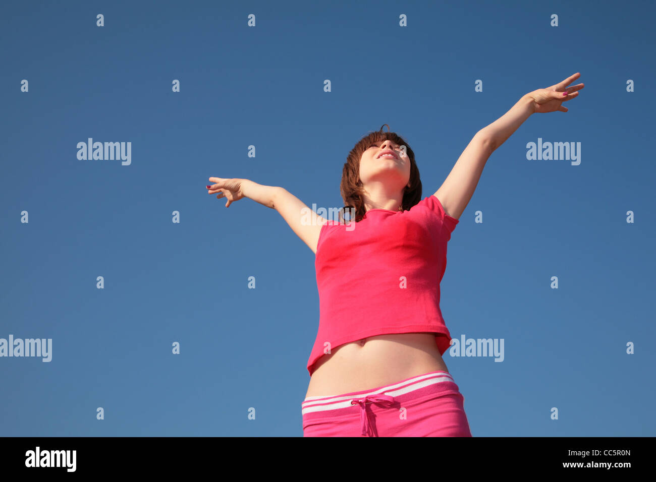 junges Mädchen mit erhobenen Händen auf blauen Himmelshintergrund Stockfoto