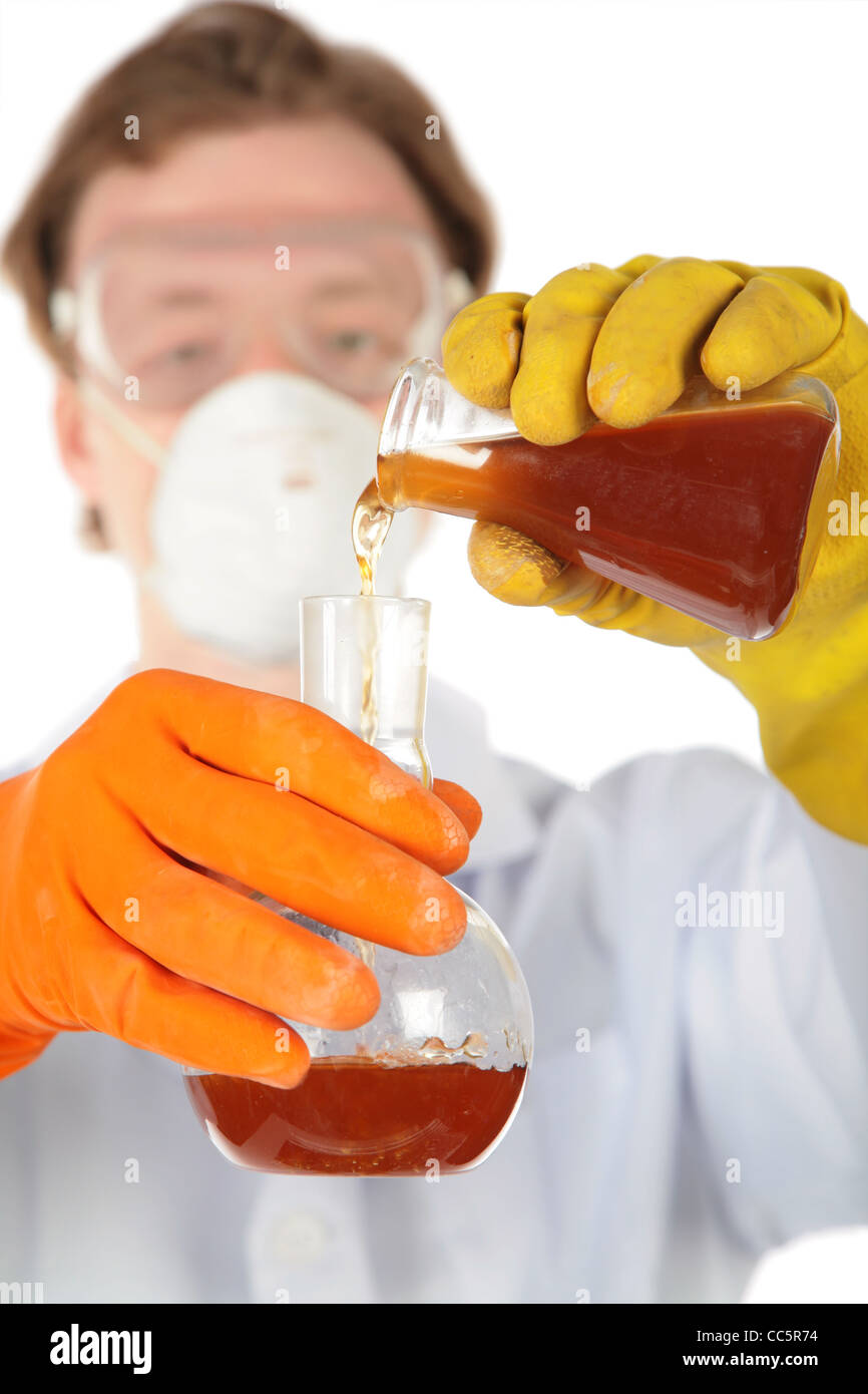 Wissenschaftler in der Atemschutzmaske und Gummihandschuhe gießt braune Flüssigkeit aus einer Flasche in einem anderen Stockfoto