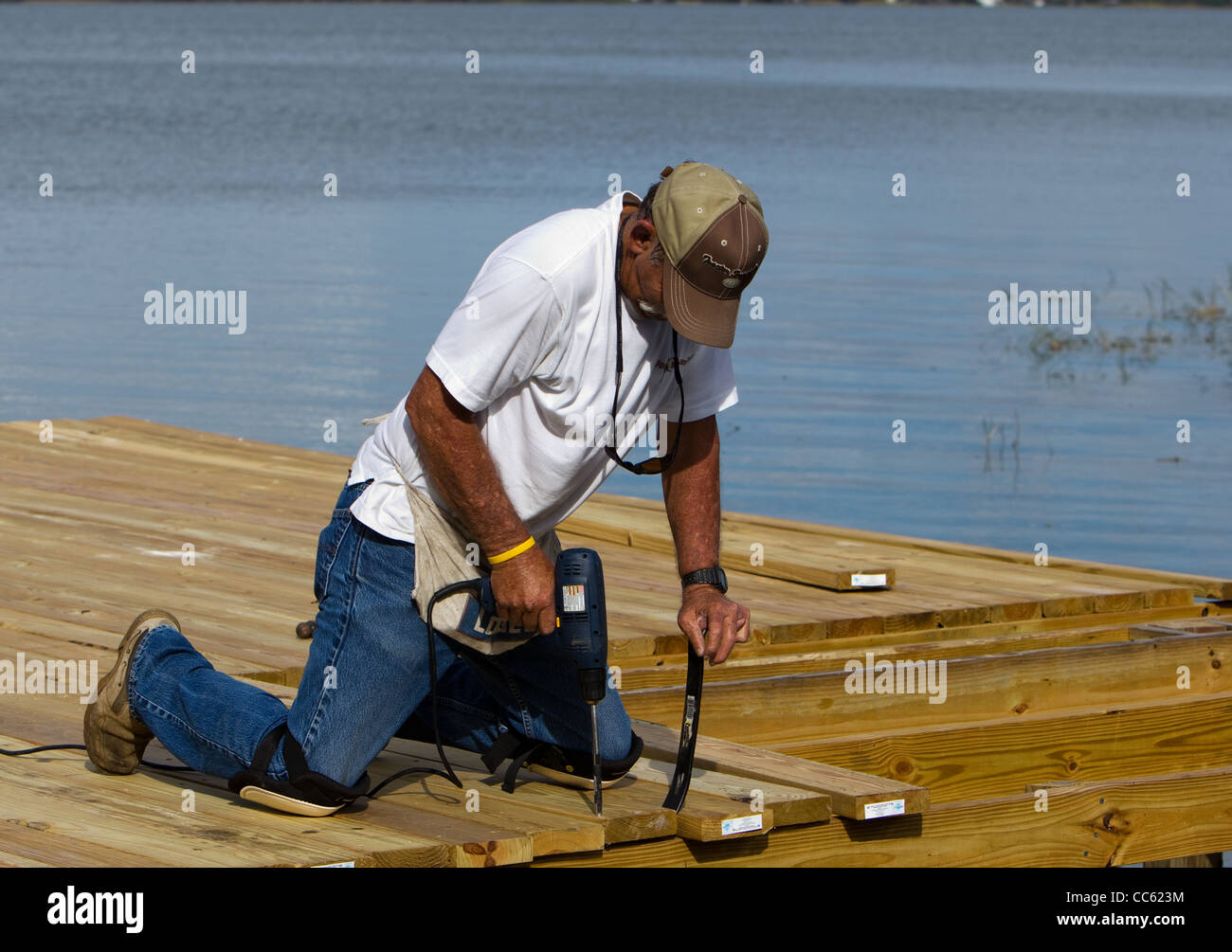 Ein Zimmermann Befestigung ein Brett nach unten auf ein Dock, über einen See mit einer elektrischen Bohrmaschine. Stockfoto