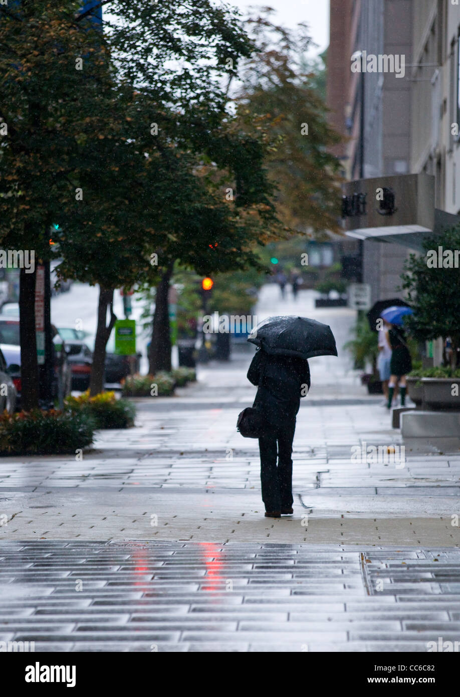 Ein Mann zu Fuß auf dem Bürgersteig mit einem Regenschirm an einem regnerischen Tag Stockfoto