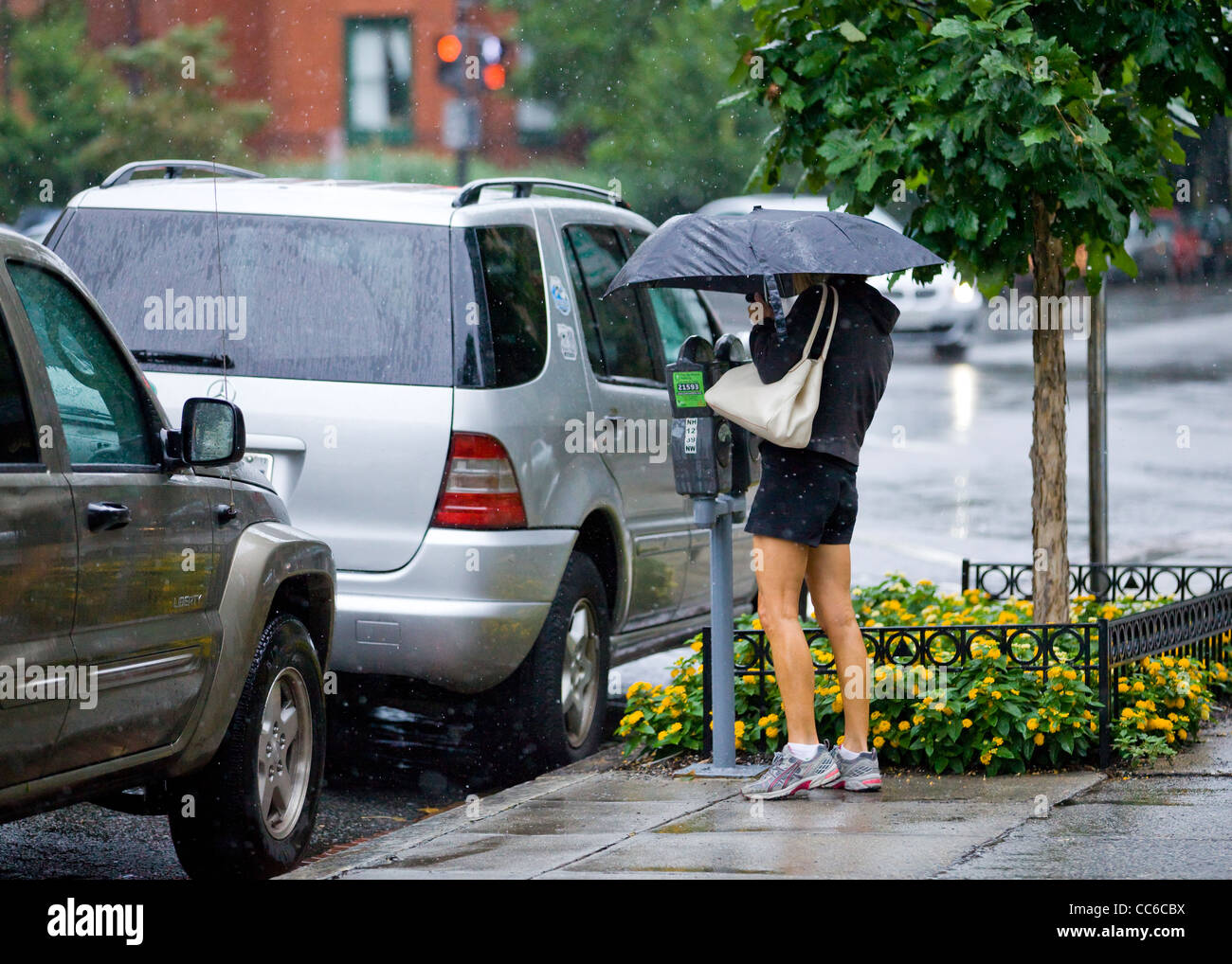 Eine Frau, die Fütterung einer Parkuhr an einem regnerischen Tag - USA Stockfoto