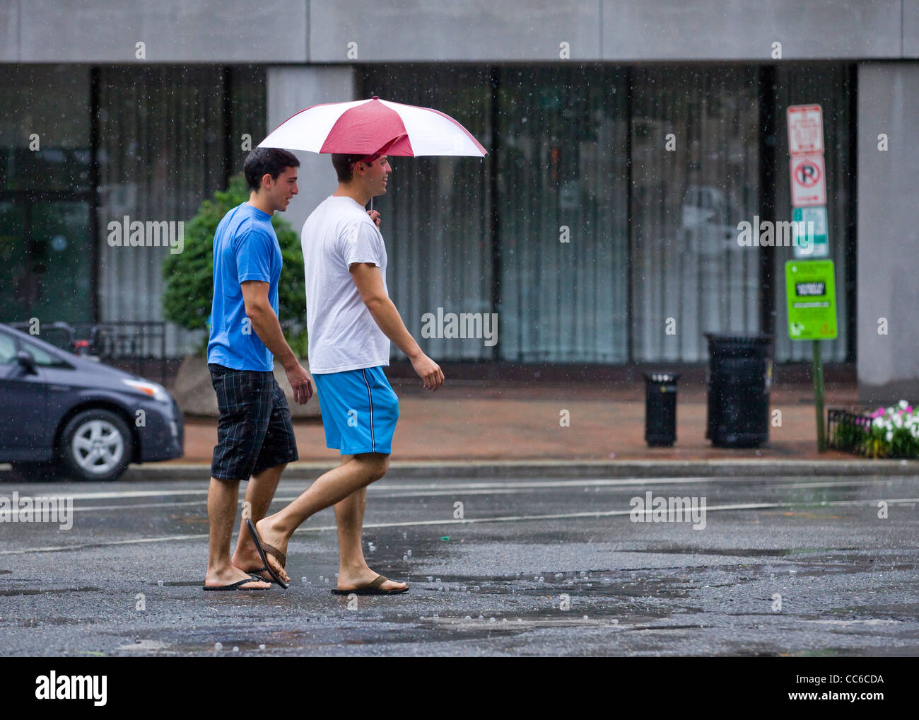 Junge Männer, die über die Straße halten einen Regenschirm an einem regnerischen Tag Stockfoto
