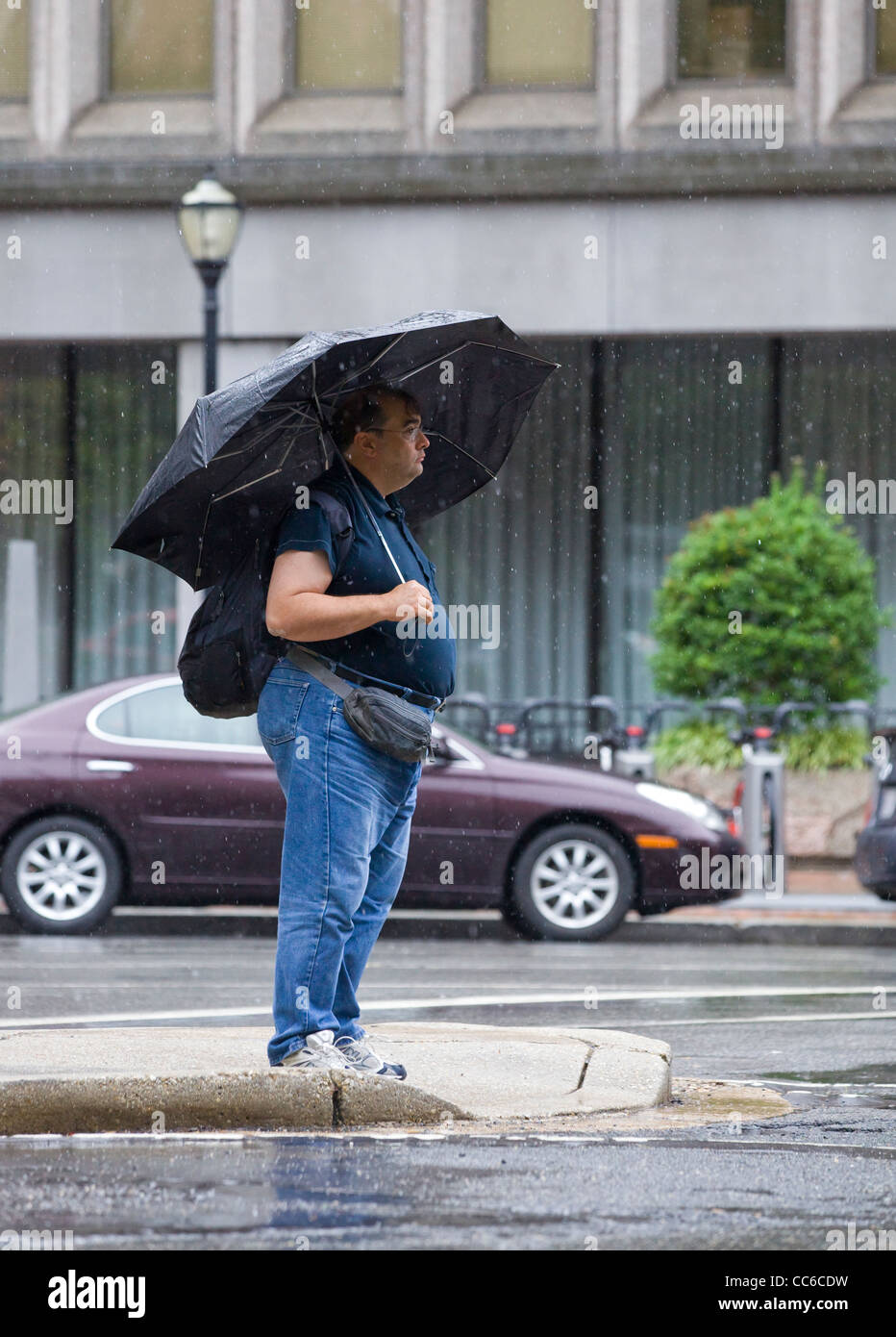 Ein Mann steht am Ende der Straße unter einem Regenschirm während ein Sturm Stockfoto