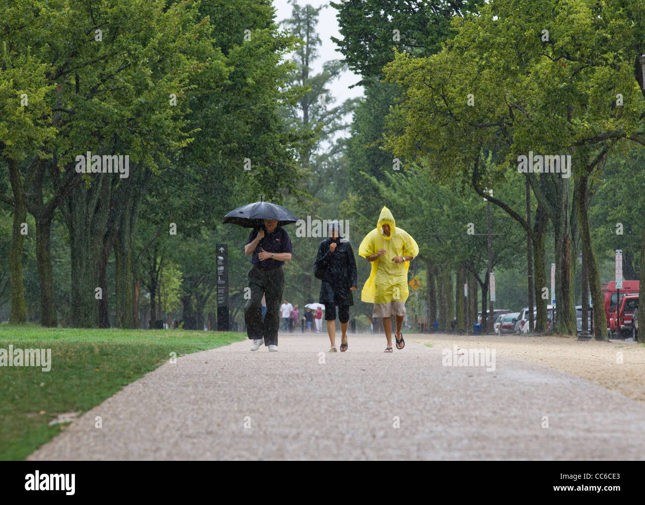Menschen, die bei starkem Regen mit Regenschirm und Regenmänteln laufen - USA Stockfoto