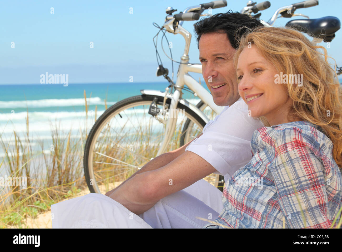 Profilbild von paar saß neben Fahrrädern am Strand Stockfoto