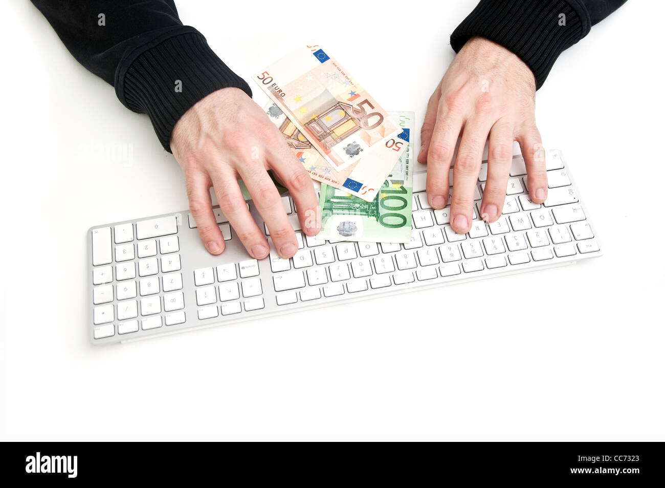 Man tippt auf Computer-Tastatur, einige Euro-Banknoten vor ihm. Stockfoto