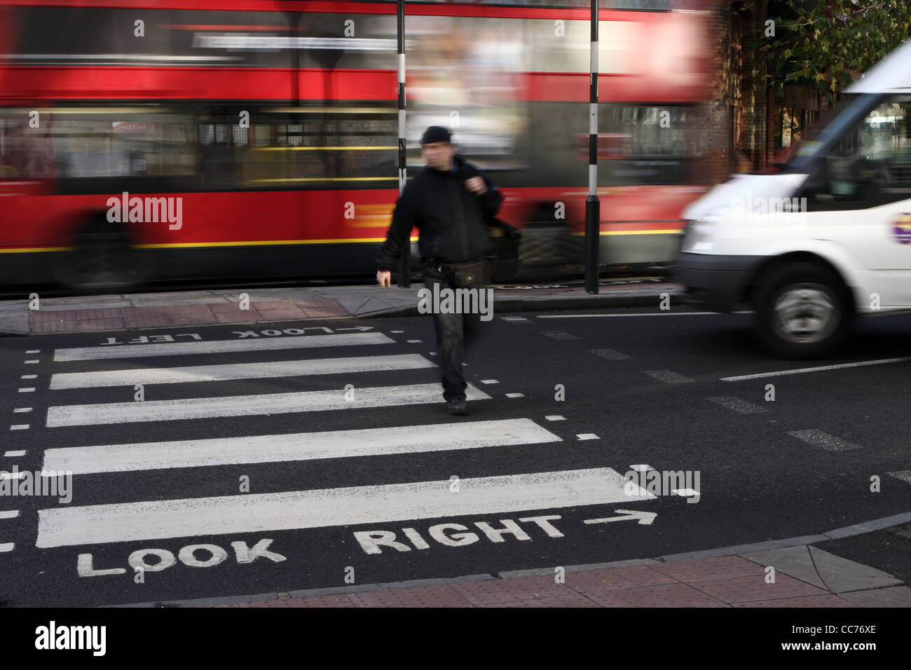 ein Mann geht über einen Zebrastreifen in London während ein weißer Lieferwagen setzt sich in Bewegung und ein Bus fährt auf der anderen Seite der Straße Stockfoto