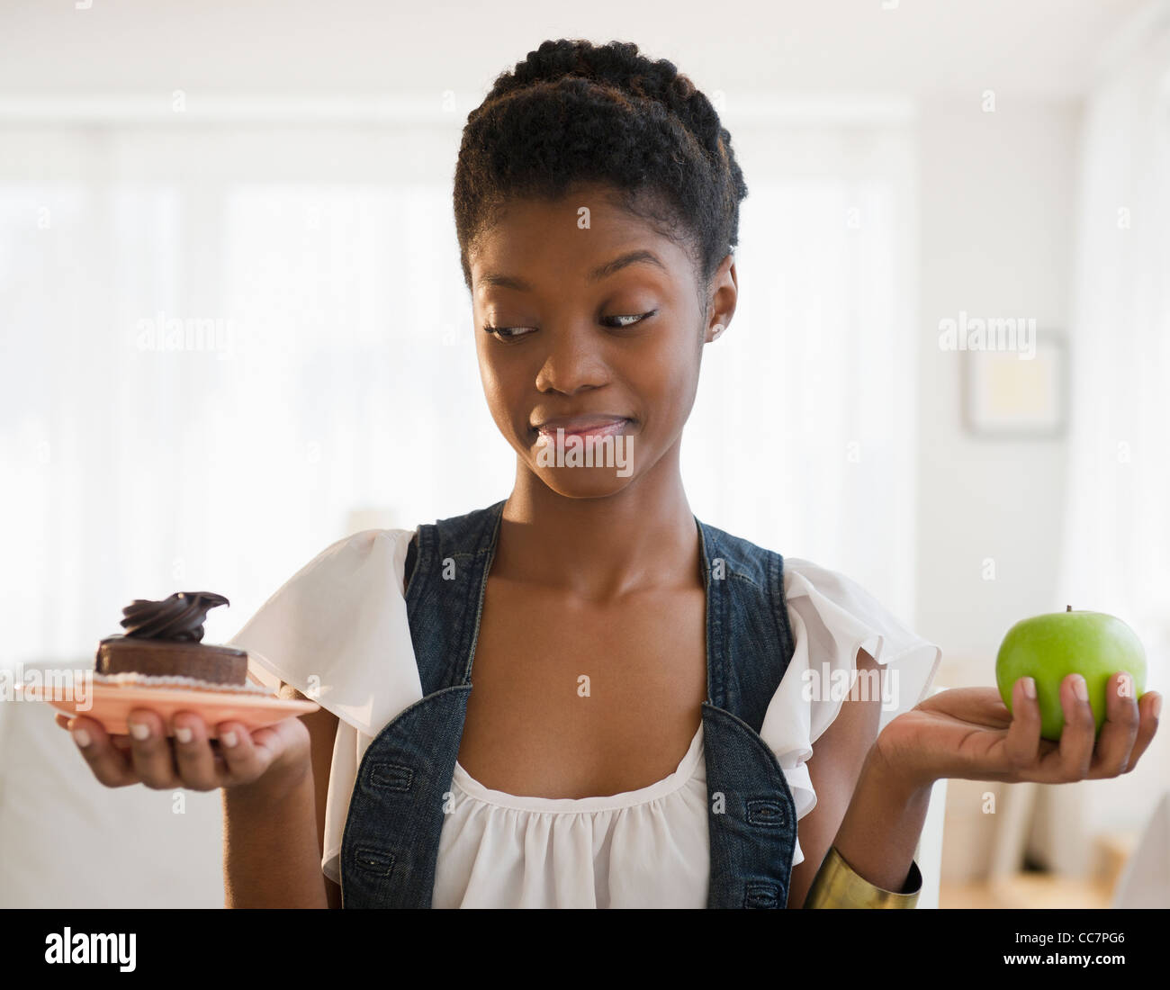 Schwarze Frau, die Entscheidung zwischen Schokoladenkuchen und Apfel Stockfoto