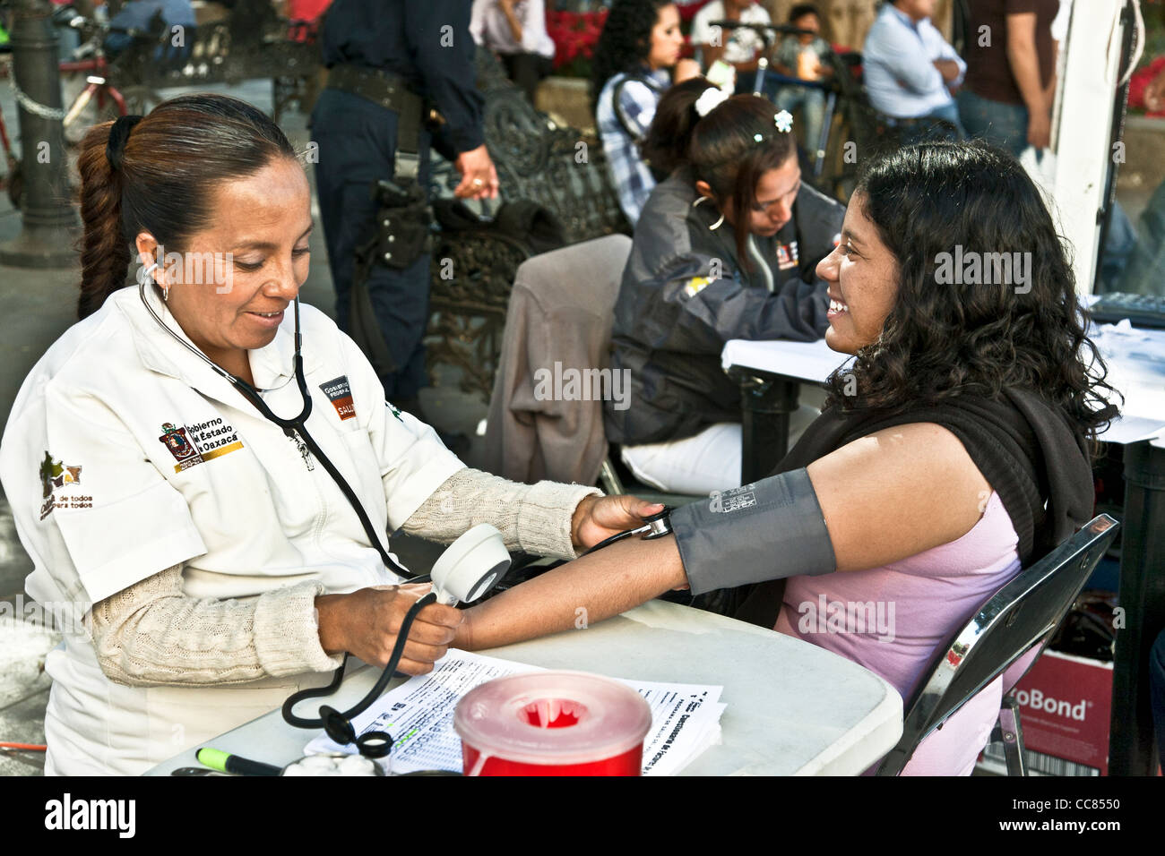 hübsche junge Mexikanerin Lächeln als Krankenschwester findet ihr Blutdruck in kostenlose Outdoor-Klinik, gesponsert vom Staat in Oaxaca Zocalo Stockfoto