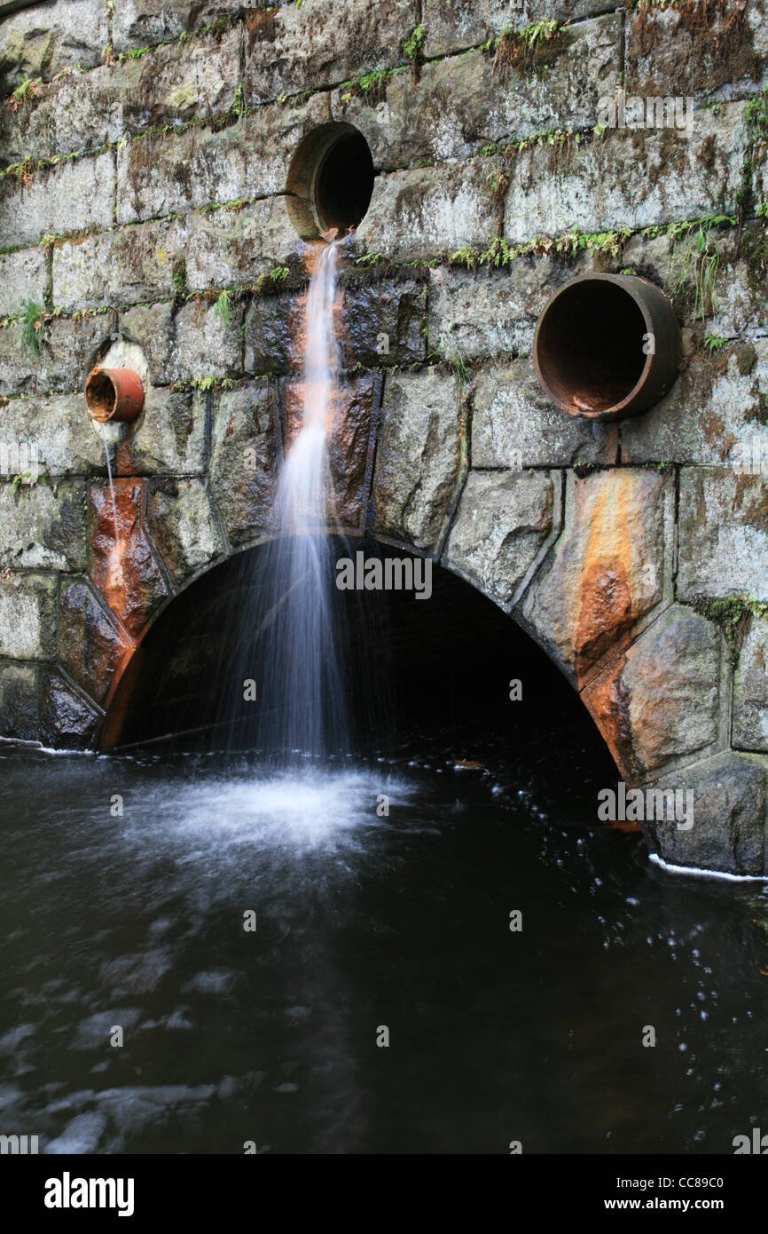 Langzeitbelichtung von Wasser aus einem Wasserablauf eine Mauer in einen Datenstrom Stockfoto