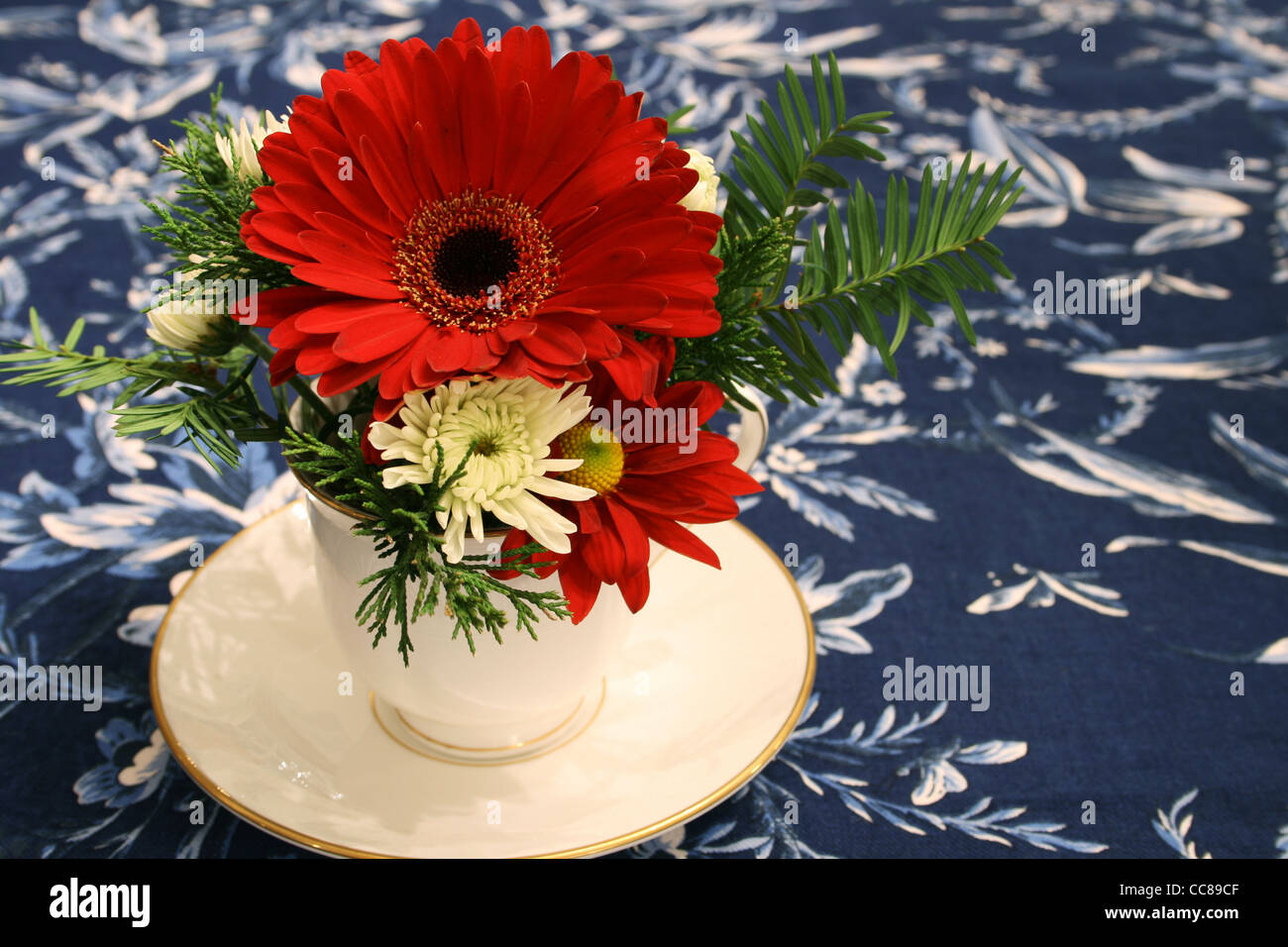 rote und weiße Blüten in eine Tasse als Herzstück auf einem blau floral Tischdecke Stockfoto