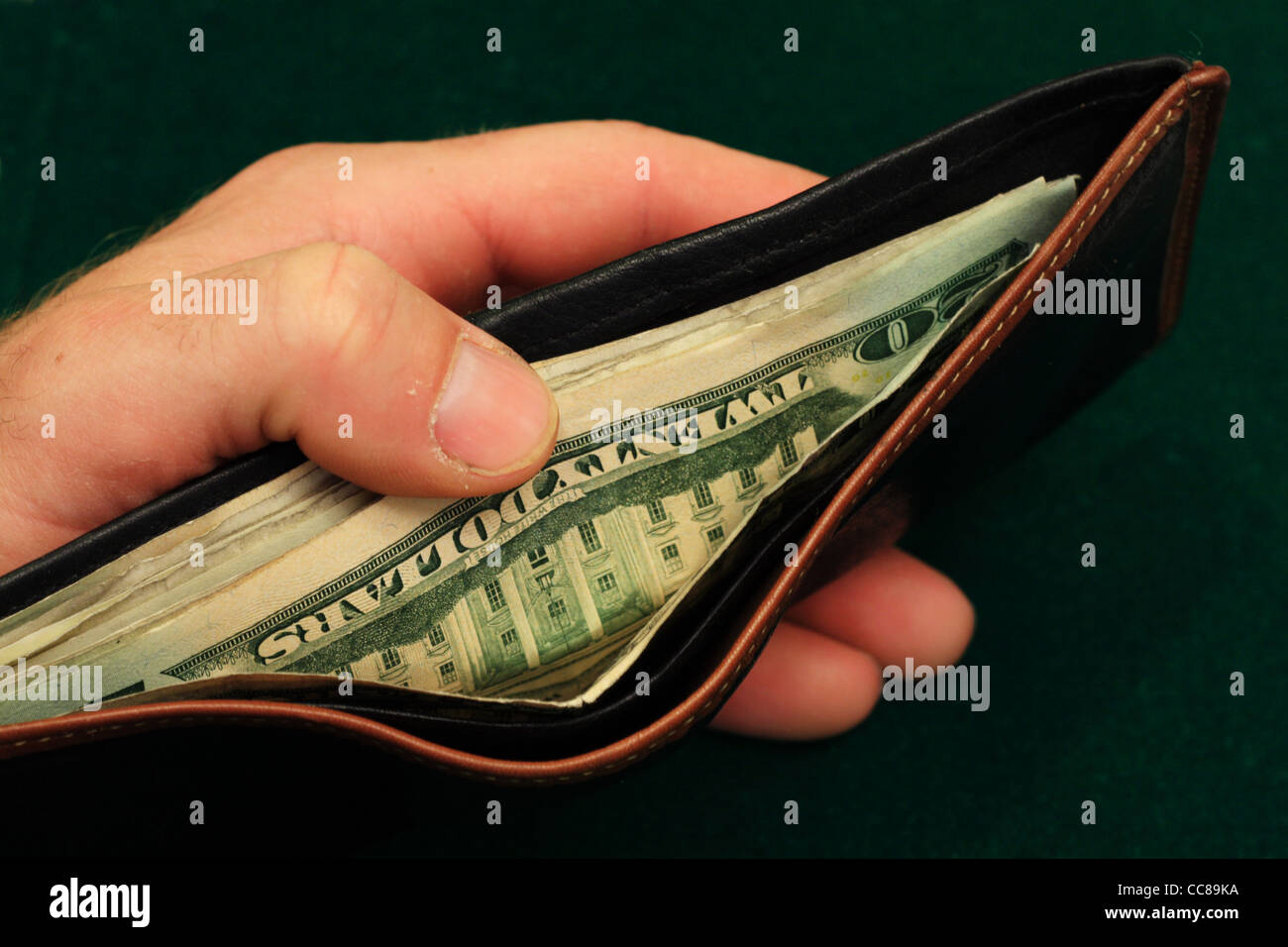 die Hand eines Mannes hält eine Leder-Portemonnaie mit US-Rechnungen offen auf einem grünen Hintergrund gefüllt Stockfoto
